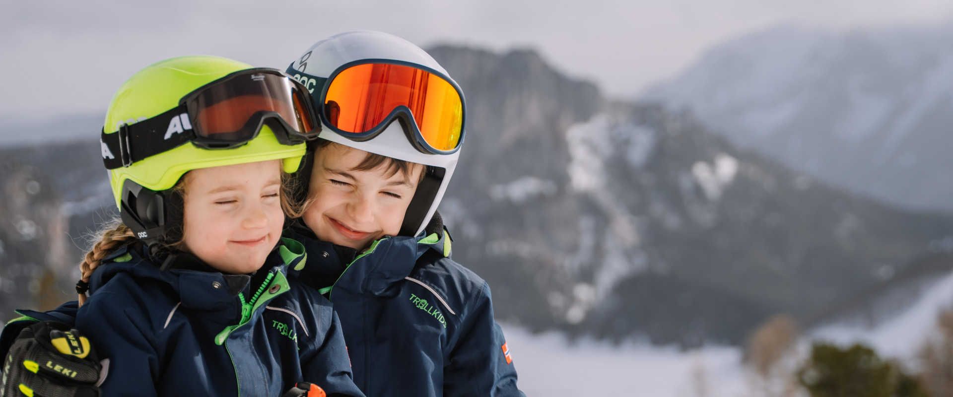 Children at the Wurzeralm in Pyhrn-Priel with their ski gear against a wintery Alpine backdrop.