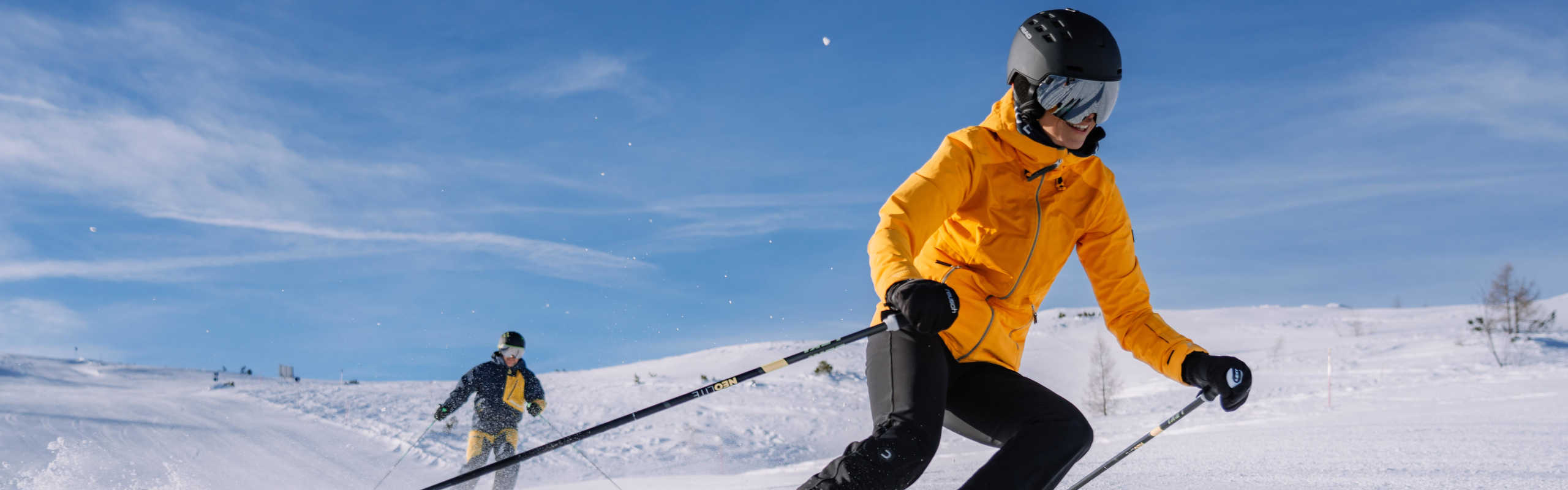 Zwei Skifahrer auf der Höss in Hinterstoder bei der Abfahrt über eine sonnige, verschneite Piste in der Region Pyhrn-Priel.