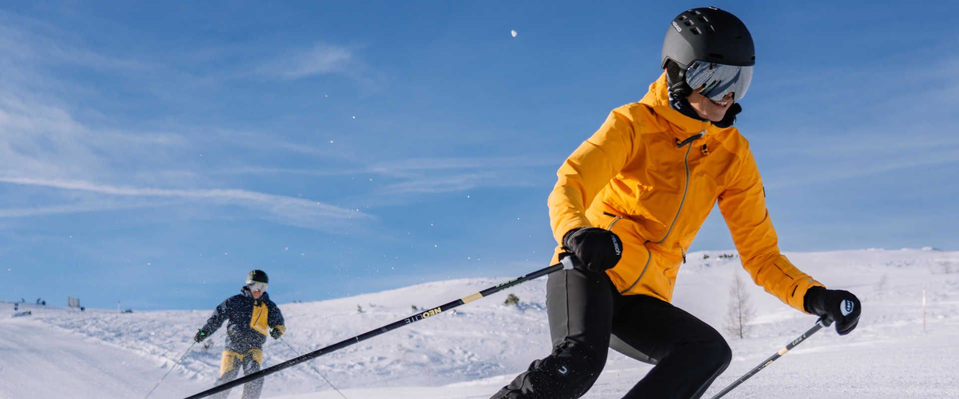 Zwei Skifahrer auf der Höss in Hinterstoder bei der Abfahrt über eine sonnige, verschneite Piste in der Region Pyhrn-Priel.