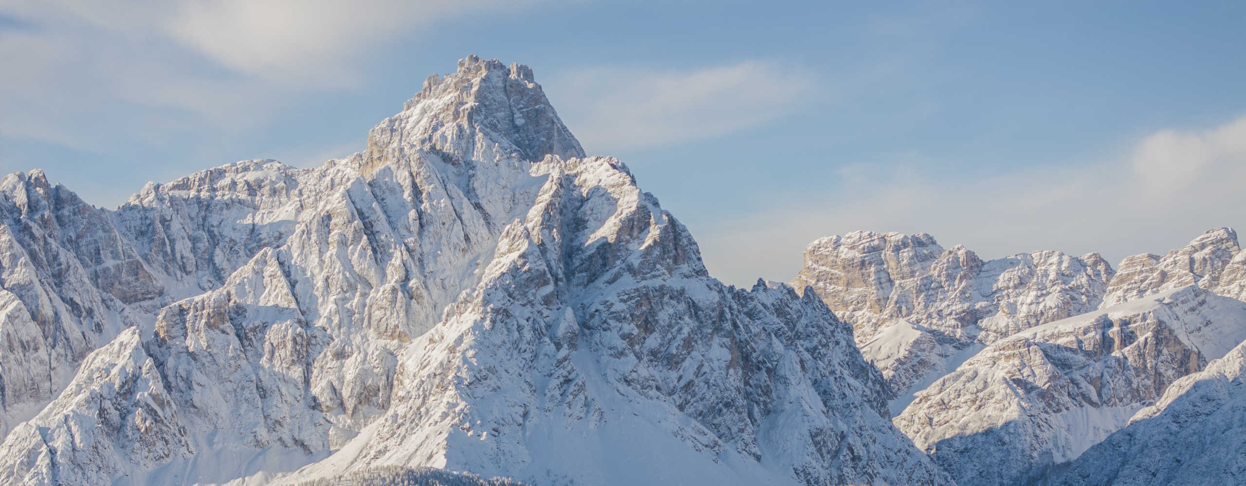 Verschneite Berggipfel der Dolomiten rund um die Drei Zinnen unter blauem Winterhimmel.