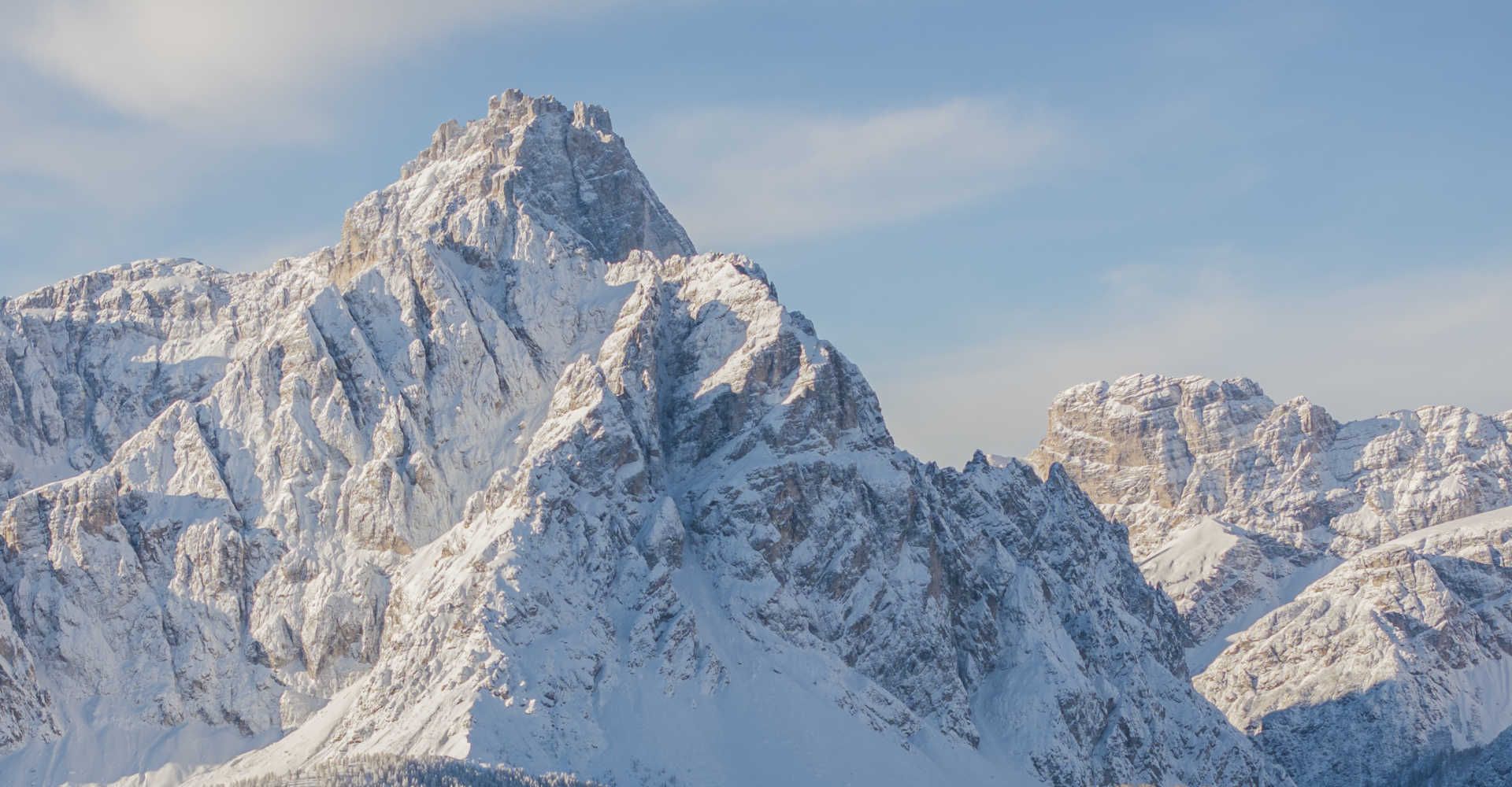 Snow-capped mountain peaks of the Dolomites surrounding the Three Peaks under a blue winter sky.