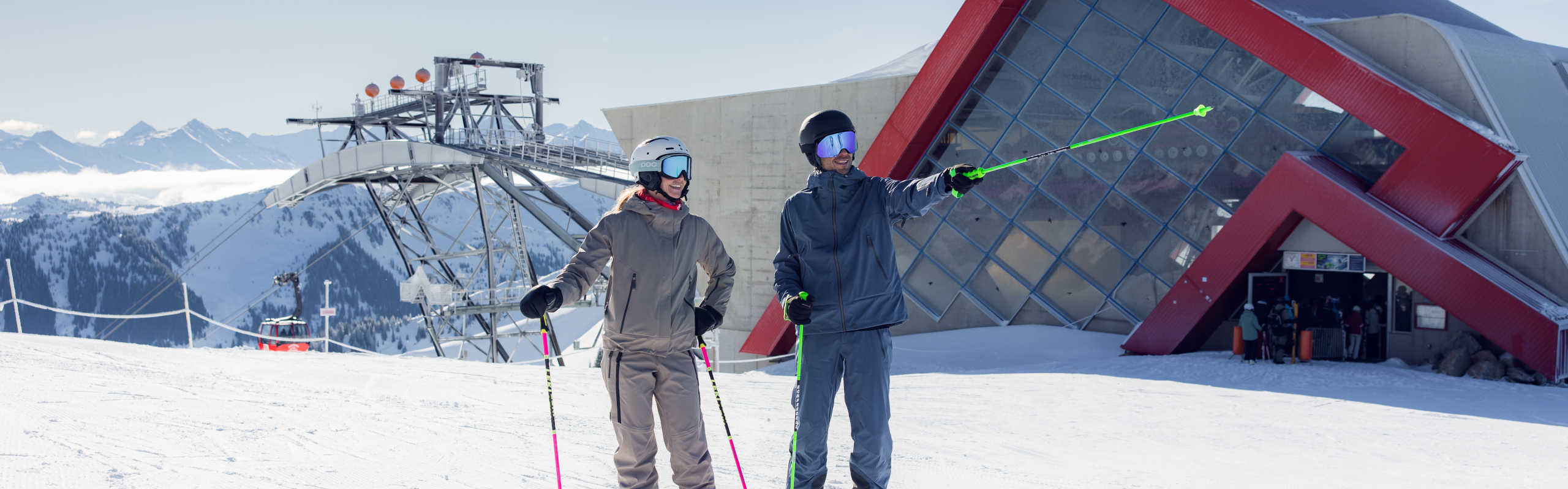 Skiers at the mountain station in Kitzbühel, featuring a modern cable car system and a panoramic view of the Alps.