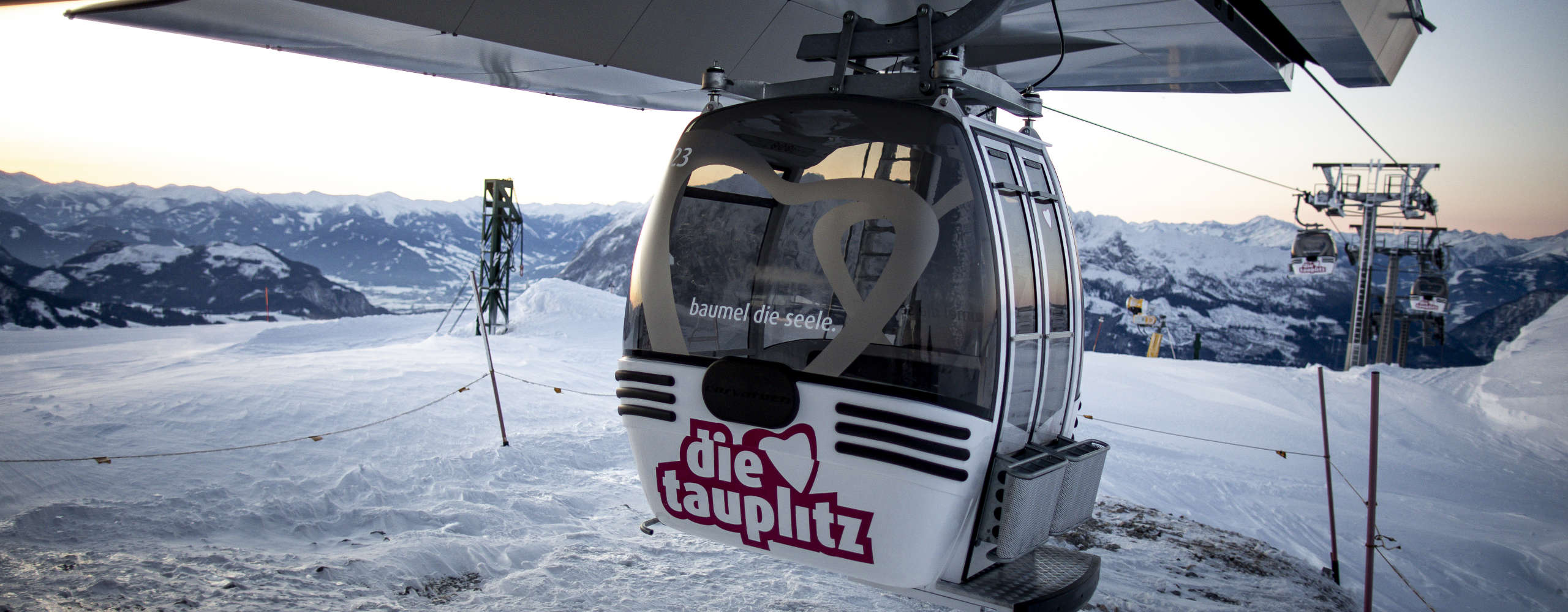 A gondola on the Tauplitzbahn in the Die Tauplitz ski resort, set against a snow-covered mountain backdrop in the Ausseerland Salzkammergut region.