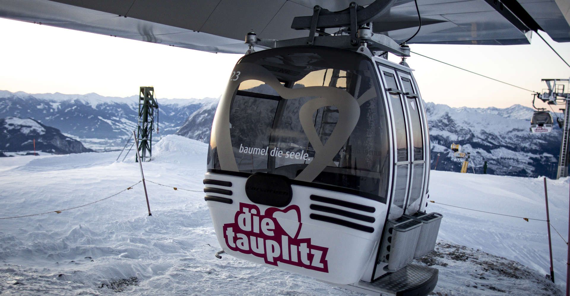A gondola on the Tauplitzbahn in the Die Tauplitz ski resort, set against a snow-covered mountain backdrop in the Ausseerland Salzkammergut region.