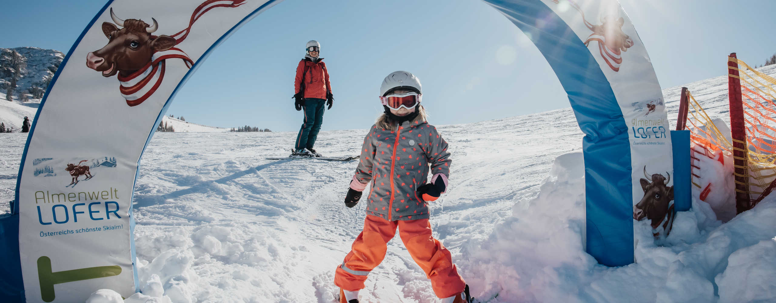 A child on skis in the children's area of Almenwelt Lofer, set against a family-friendly winter landscape.
