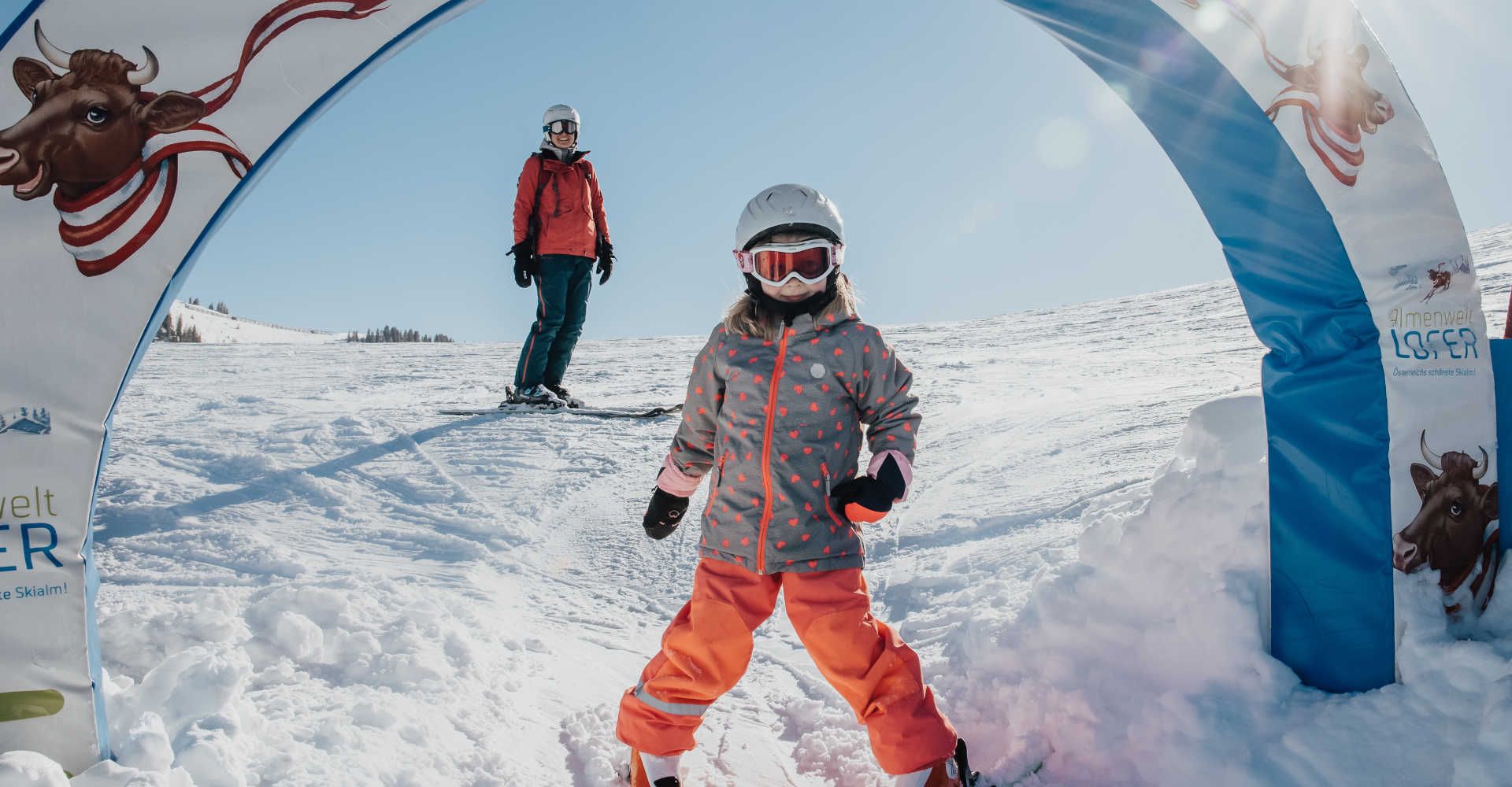 A child on skis in the children's area of Almenwelt Lofer, set against a family-friendly winter landscape.
