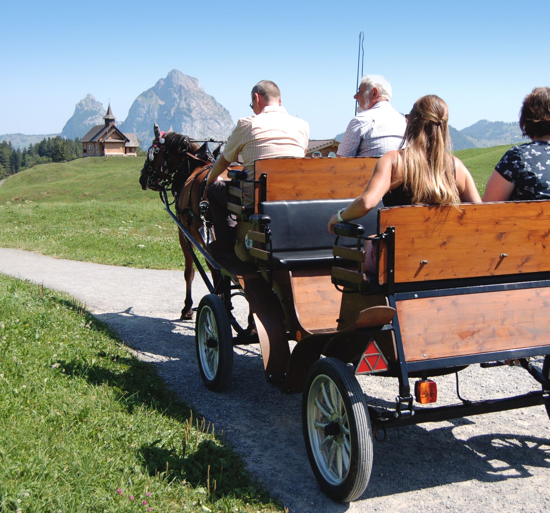 Gruppe fährt mit einer Pferdekutsche auf einem Bergweg durch eine alpine Landschaft.