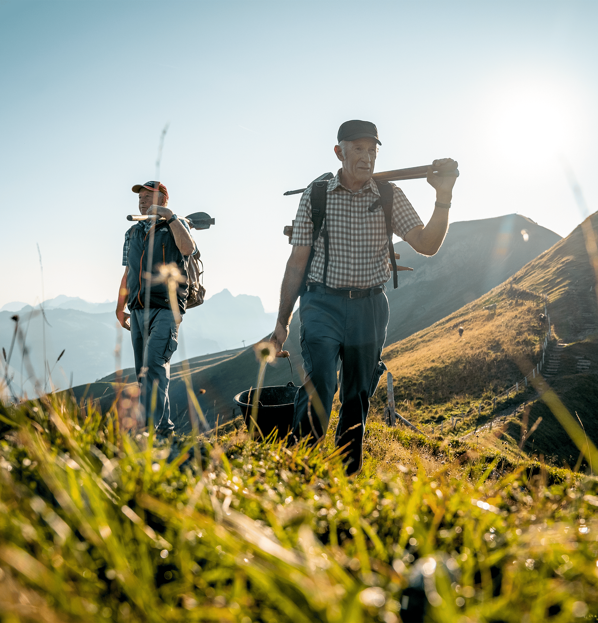 Two hikers walking through a mountain meadow in warm light with views of the surrounding mountains.