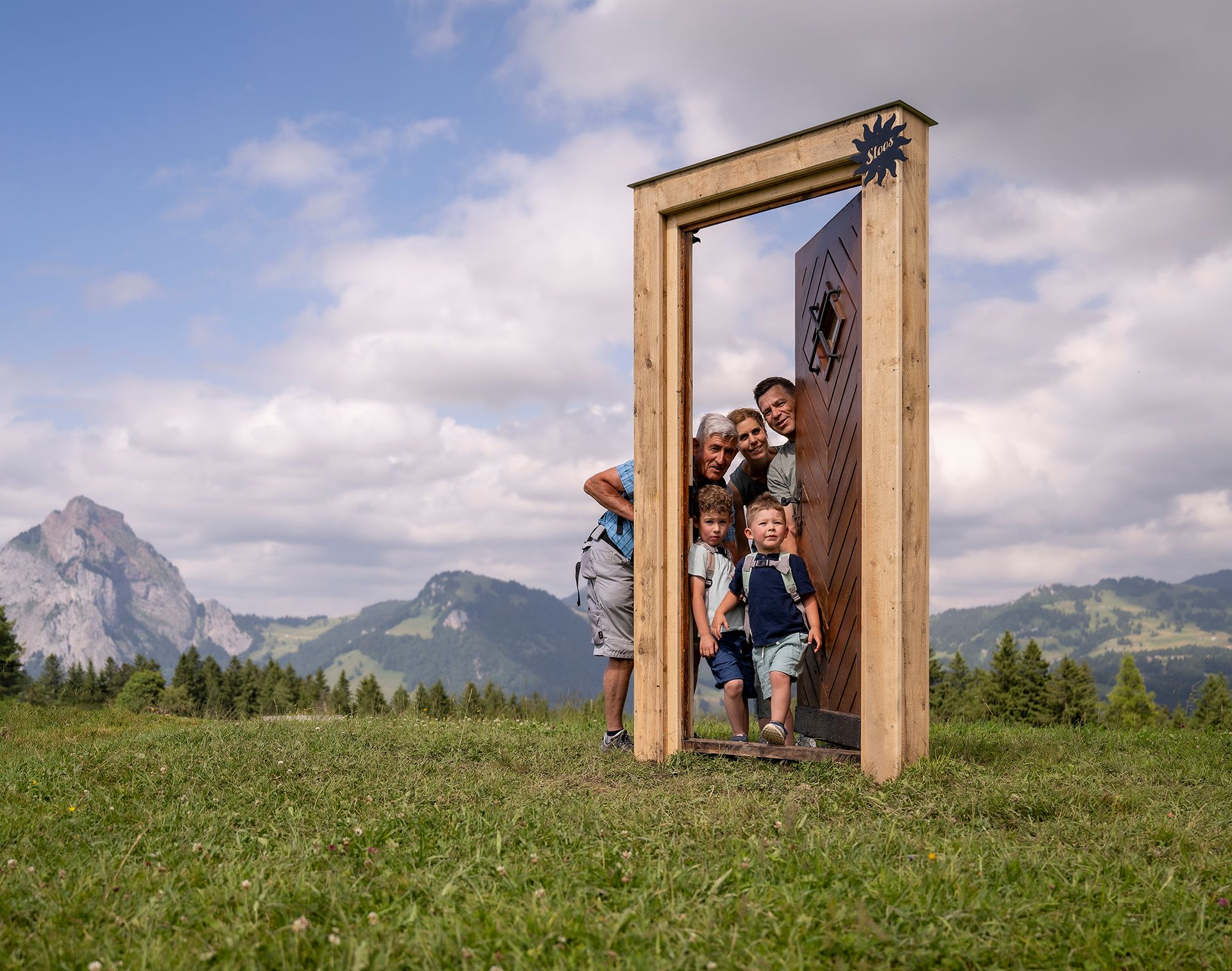 Family posing in an oversized wooden door in an alpine landscape with mountain views.