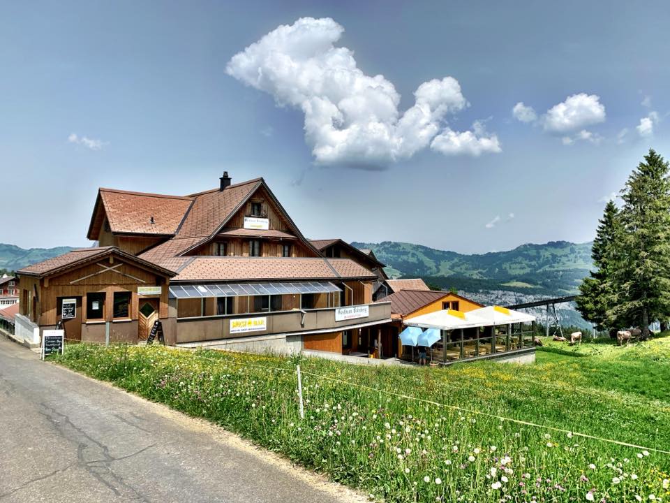 Bergrestaurant mit Terrasse auf einer Wiese in alpiner Landschaft.