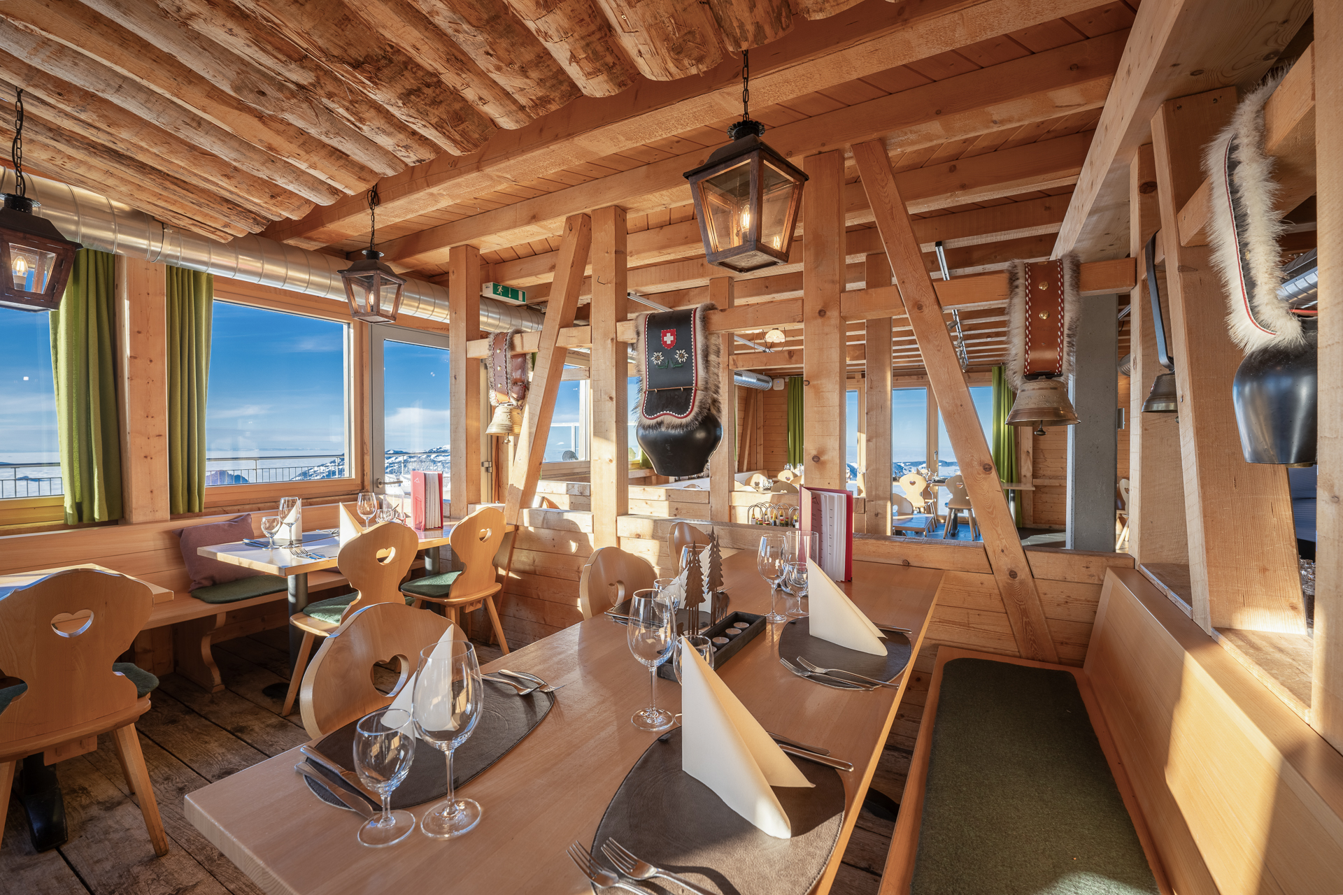 Gemütlicher Restaurantbereich mit viel Holz, gedeckten Tischen und Blick auf die Berglandschaft.