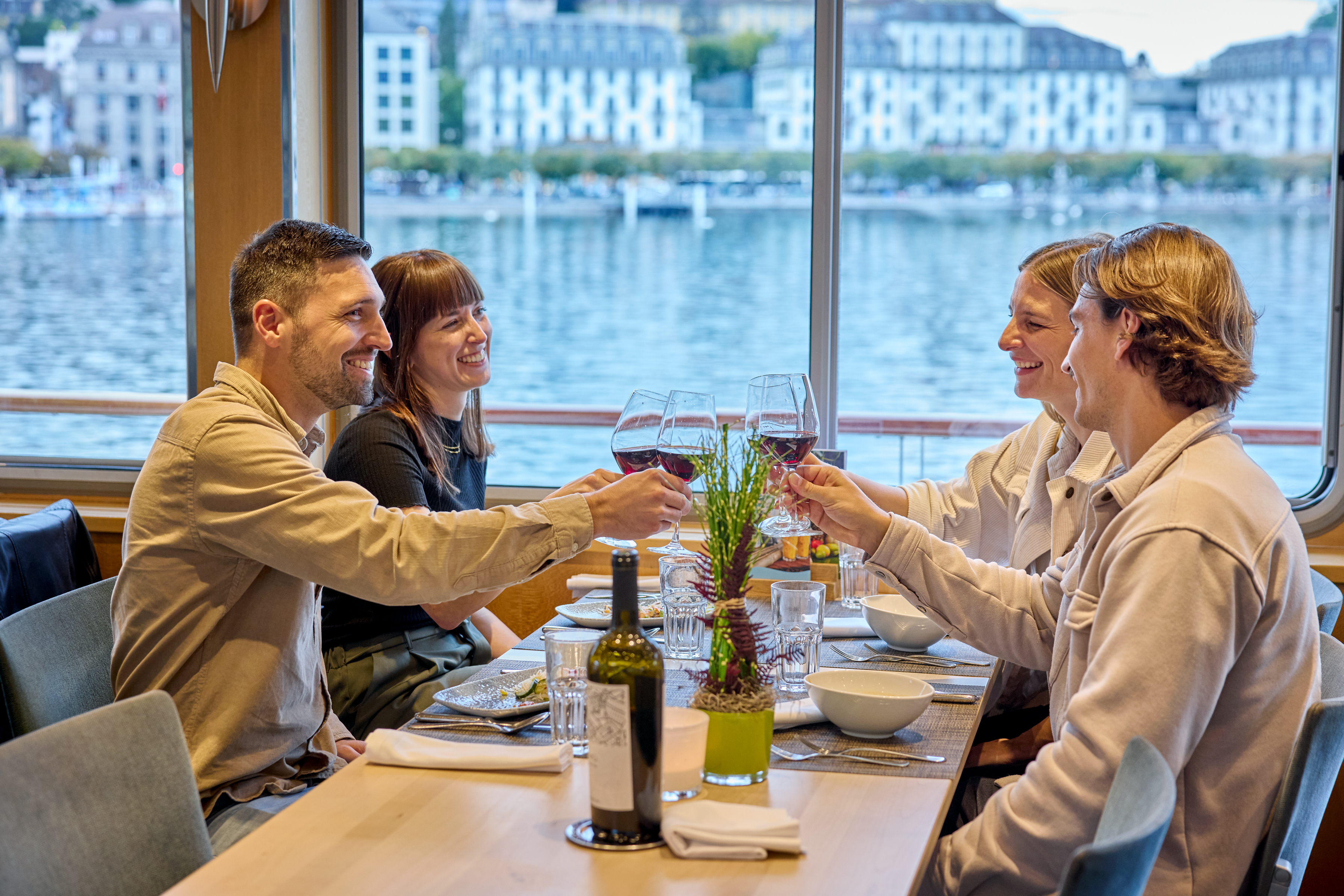 Gruppe von Gästen stösst mit Gläsern bei einem Abendessen an Bord eines Schiffes an.