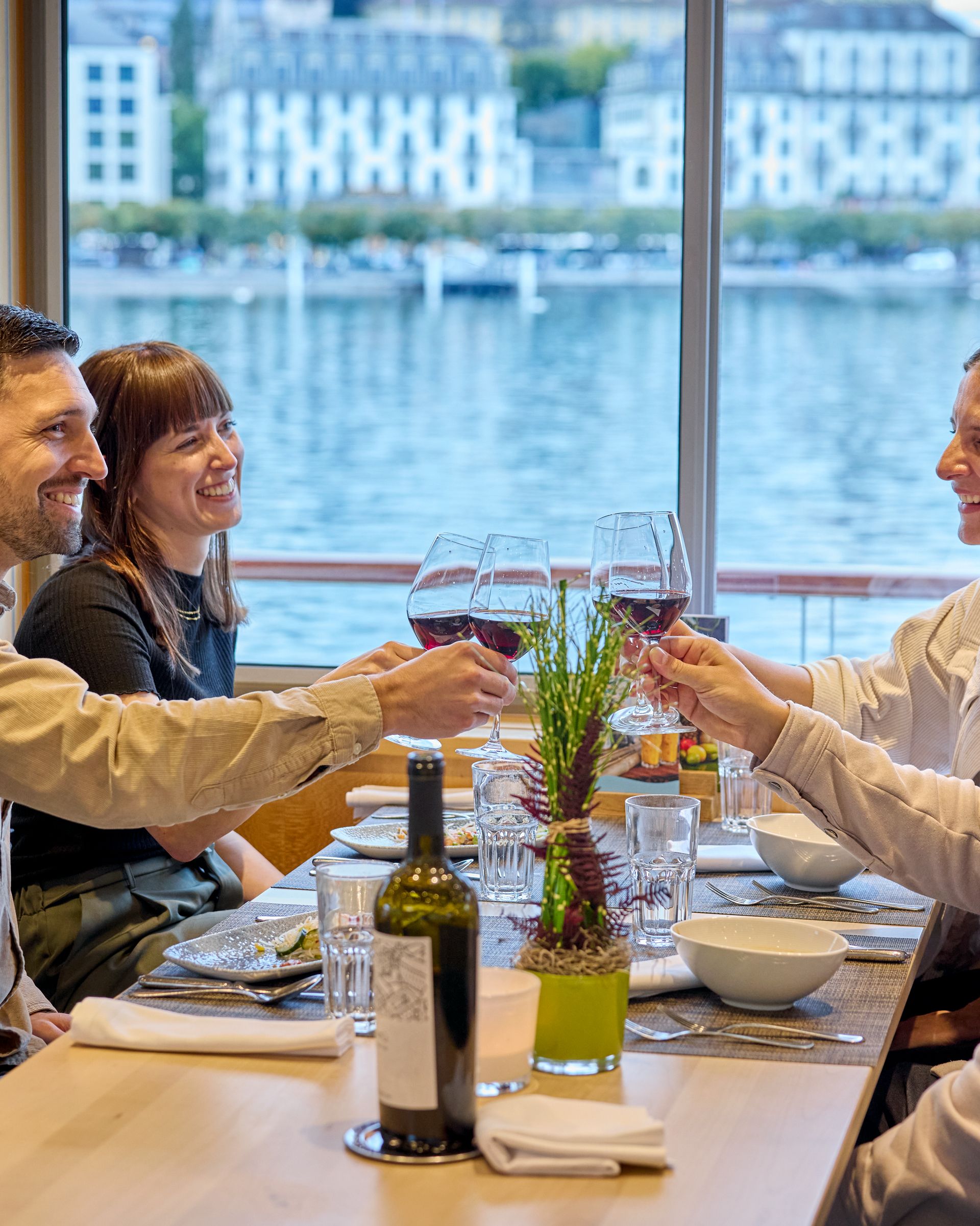 Gruppe von Gästen stösst mit Gläsern bei einem Abendessen an Bord eines Schiffes an.