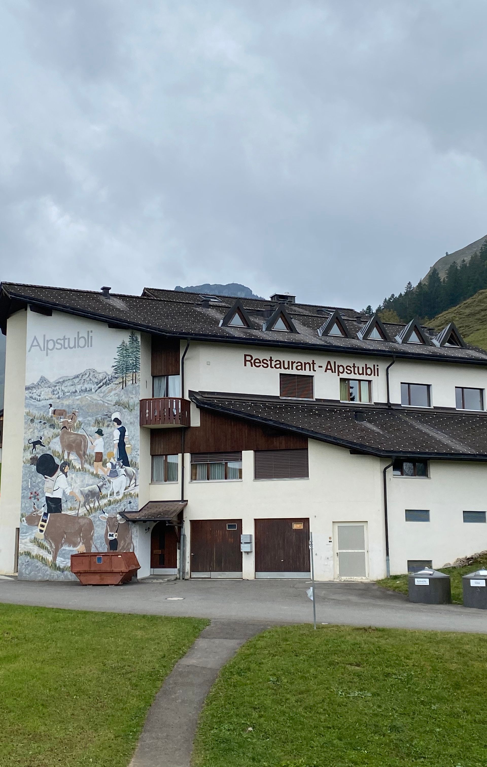 Bergrestaurant mit grosser Fassadenmalerei in alpiner Landschaft.