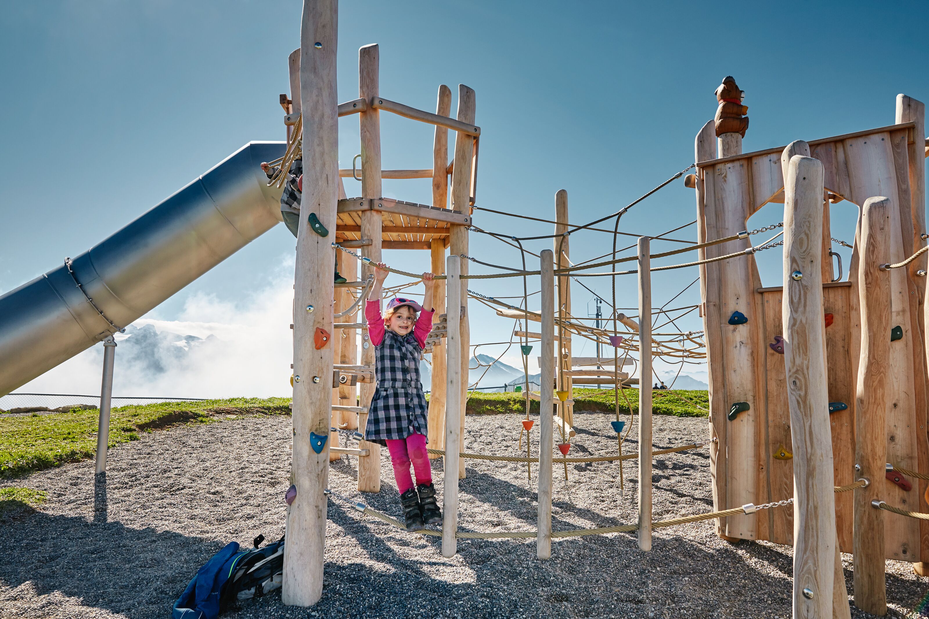 Child climbing on a wooden playground in an alpine setting.