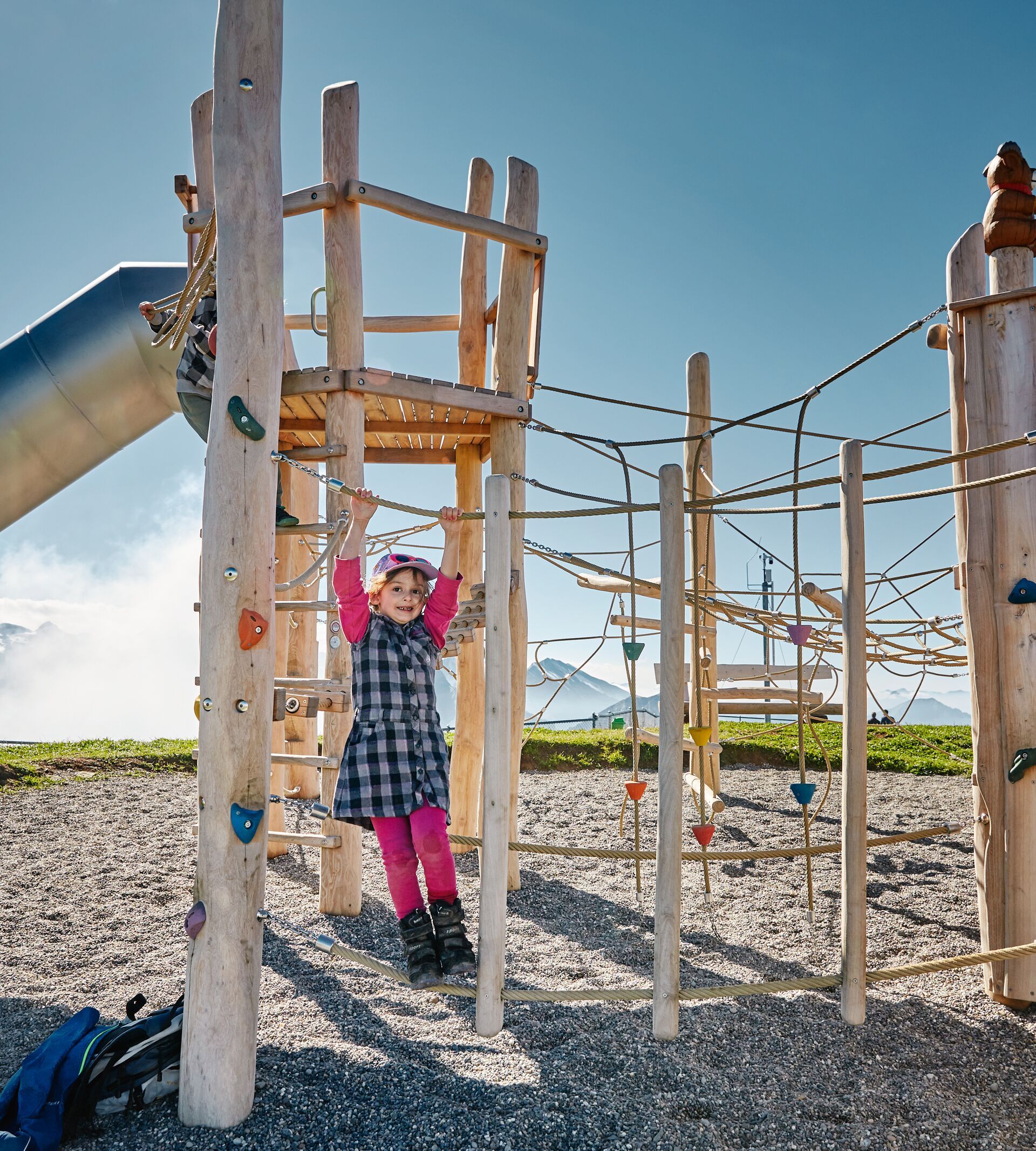 Kind klettert auf einem Holzspielplatz in alpiner Umgebung.