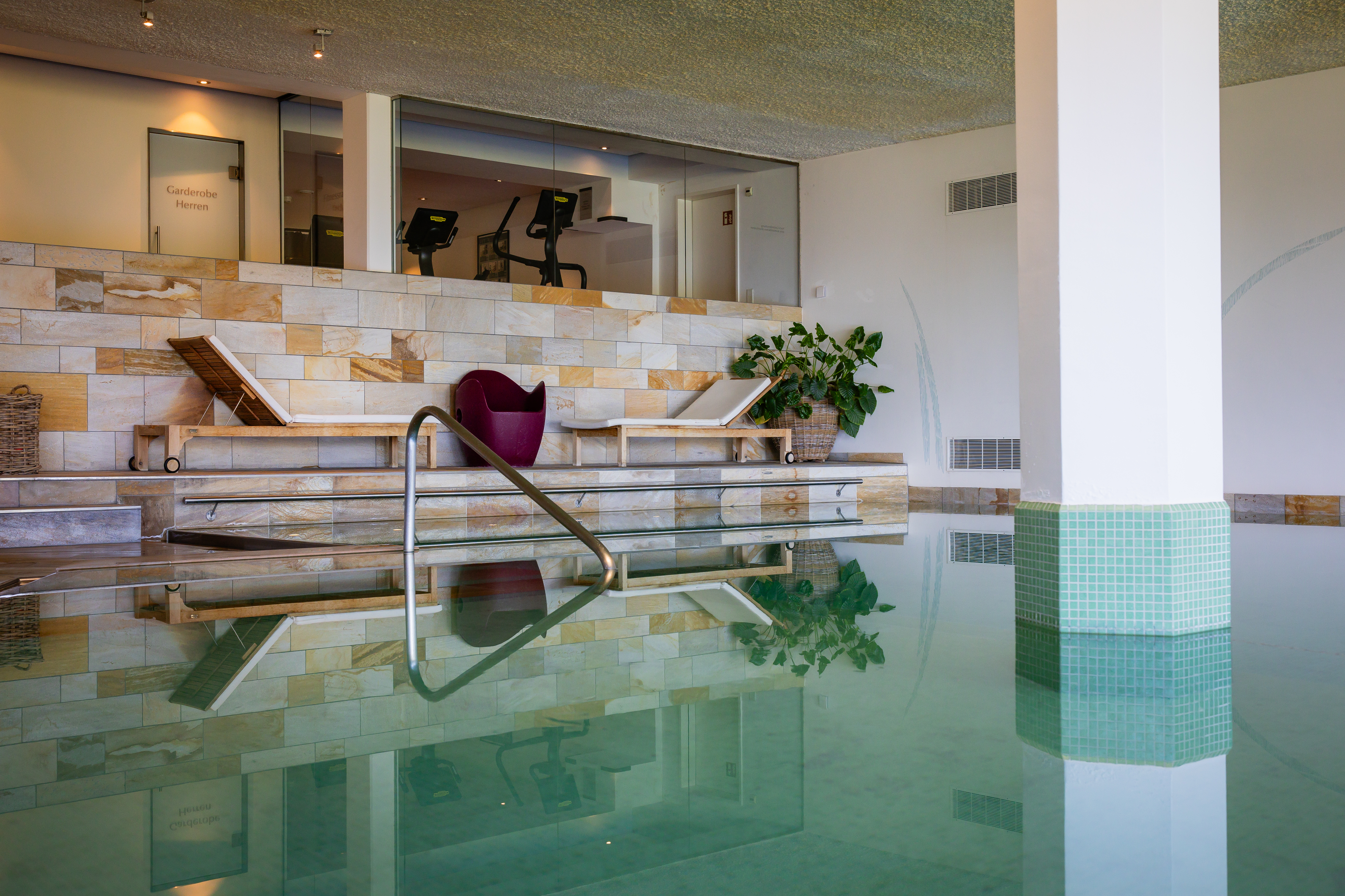 Modern indoor pool with large swimming area, seating lounge with chairs and plants in the background