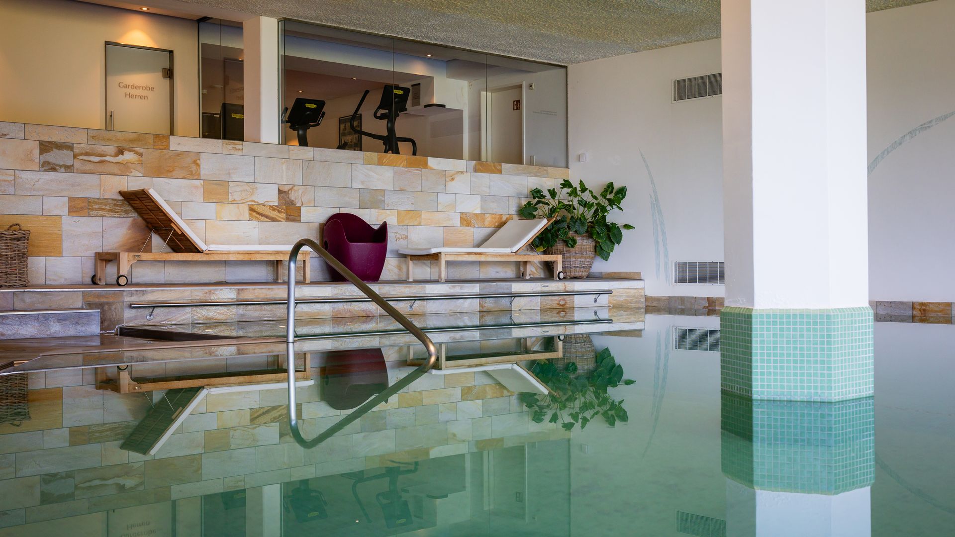 Modern indoor pool with large swimming area, seating lounge with chairs and plants in the background