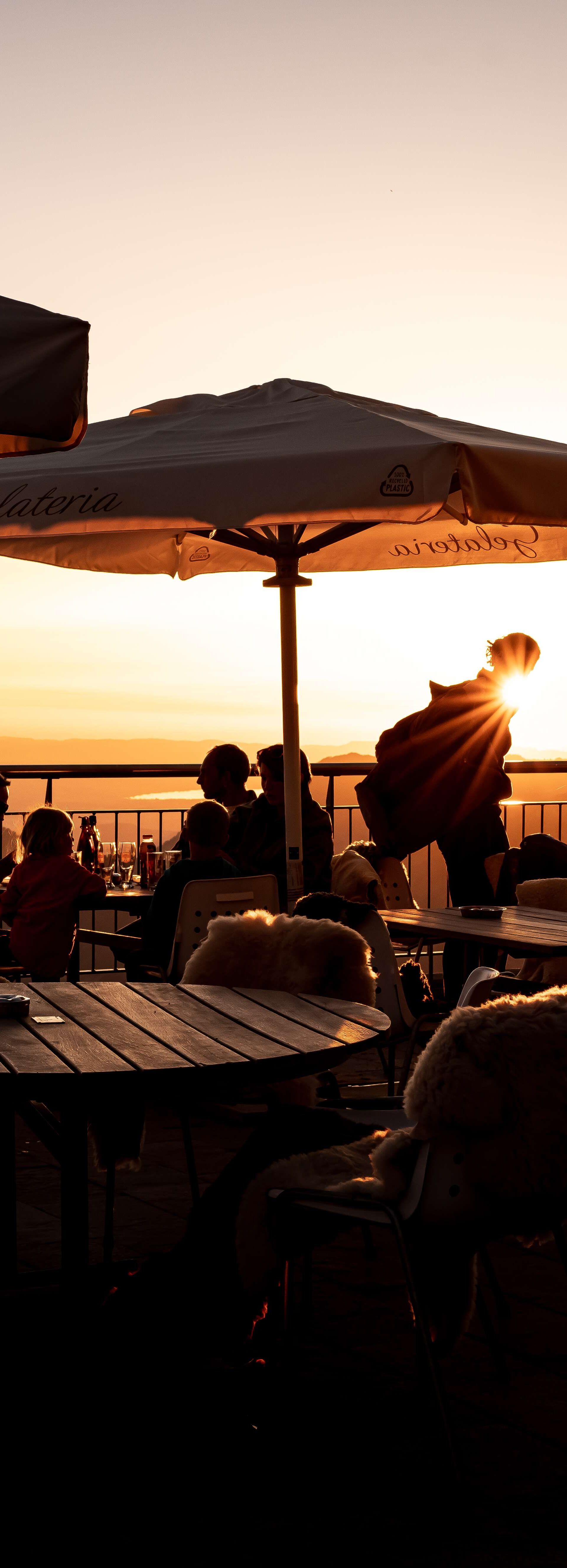 Restaurantterrasse im Sonnenuntergang mit Gästen und Blick auf die Berglandschaft.
