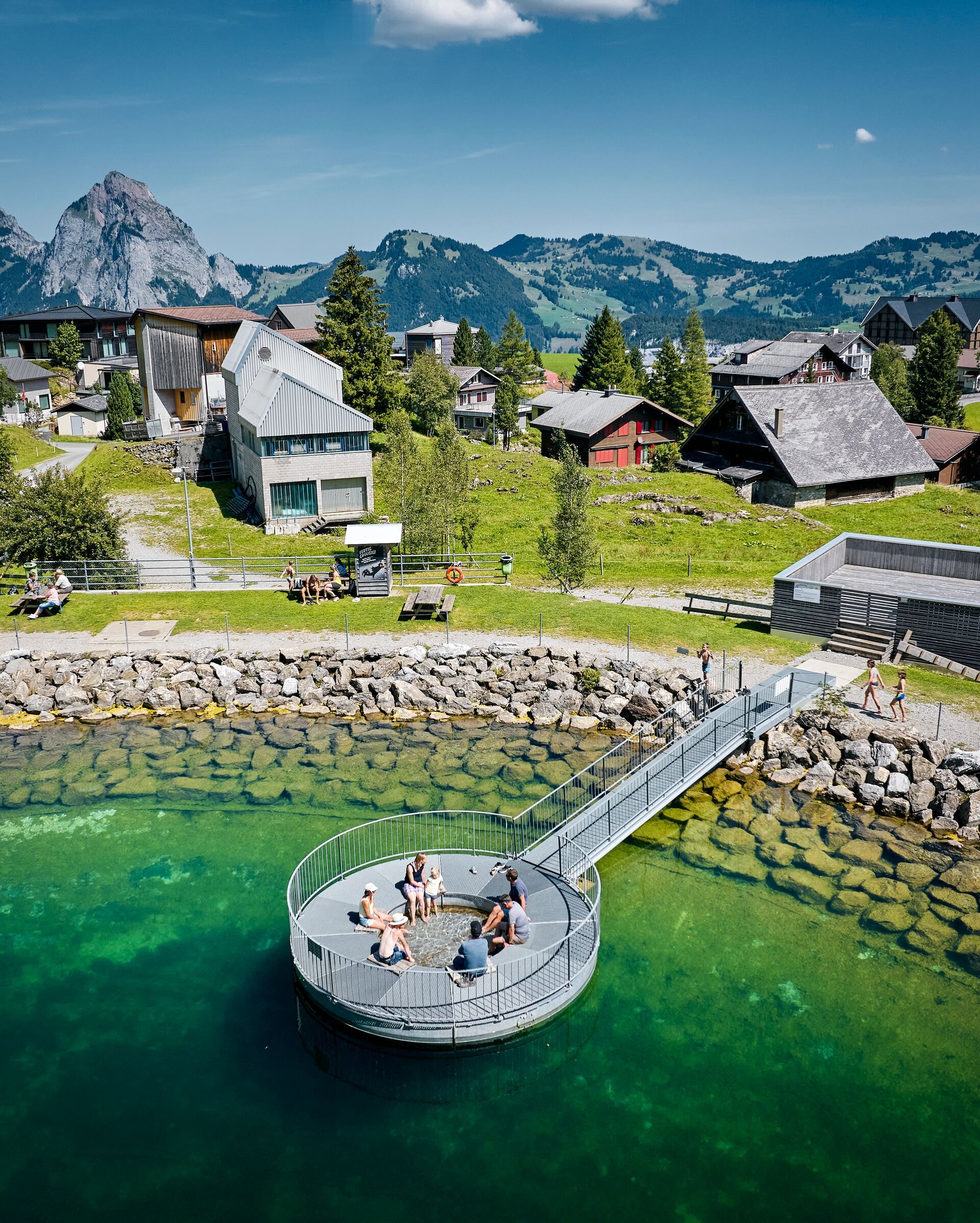 Stoos mountain village with houses, a chapel, and a mountain lake in an alpine landscape.
