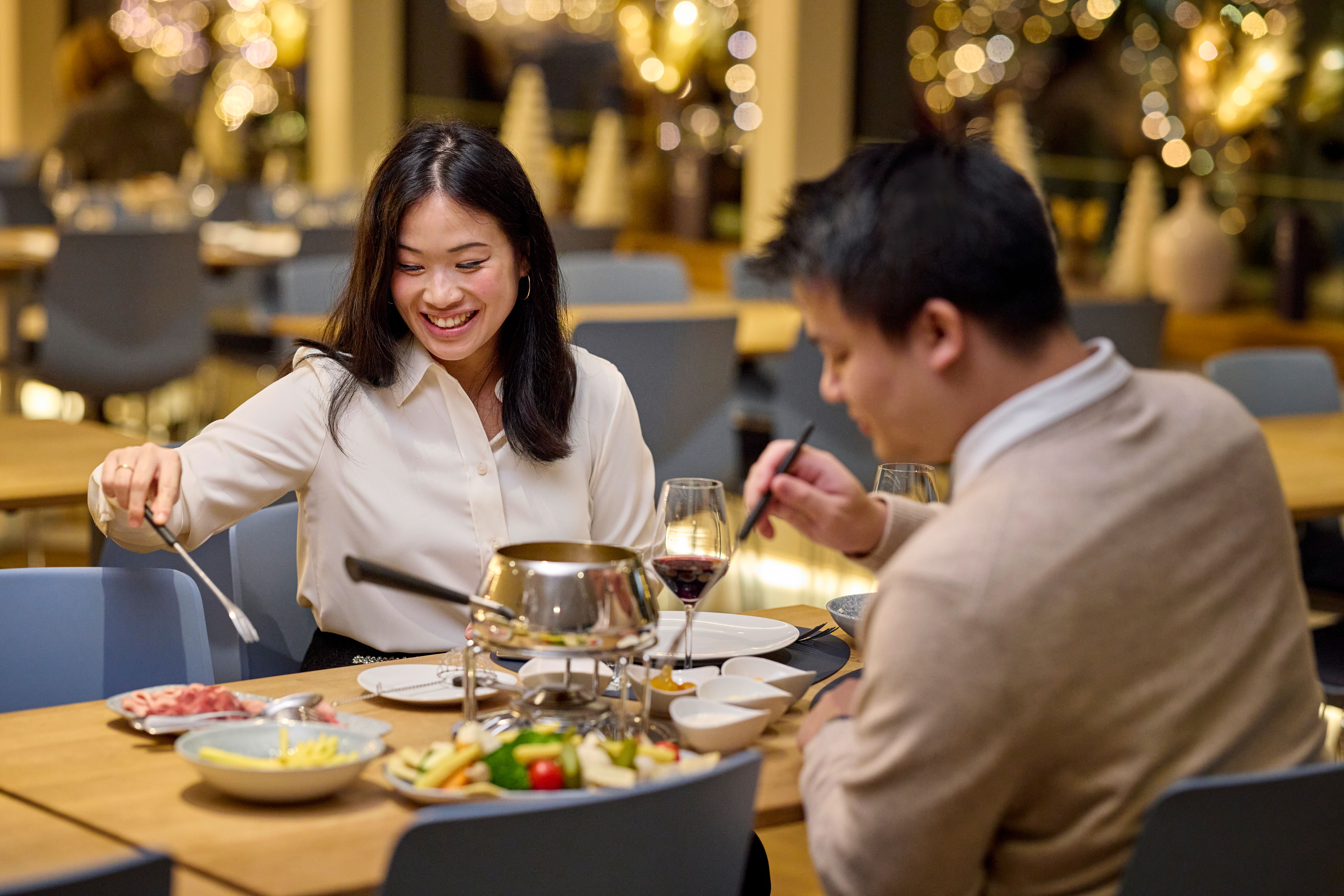 Paar sitzt an einem Tisch und bereitet Fondue Chinoise in einem Topf im Innenraum eines Schiffes zu.