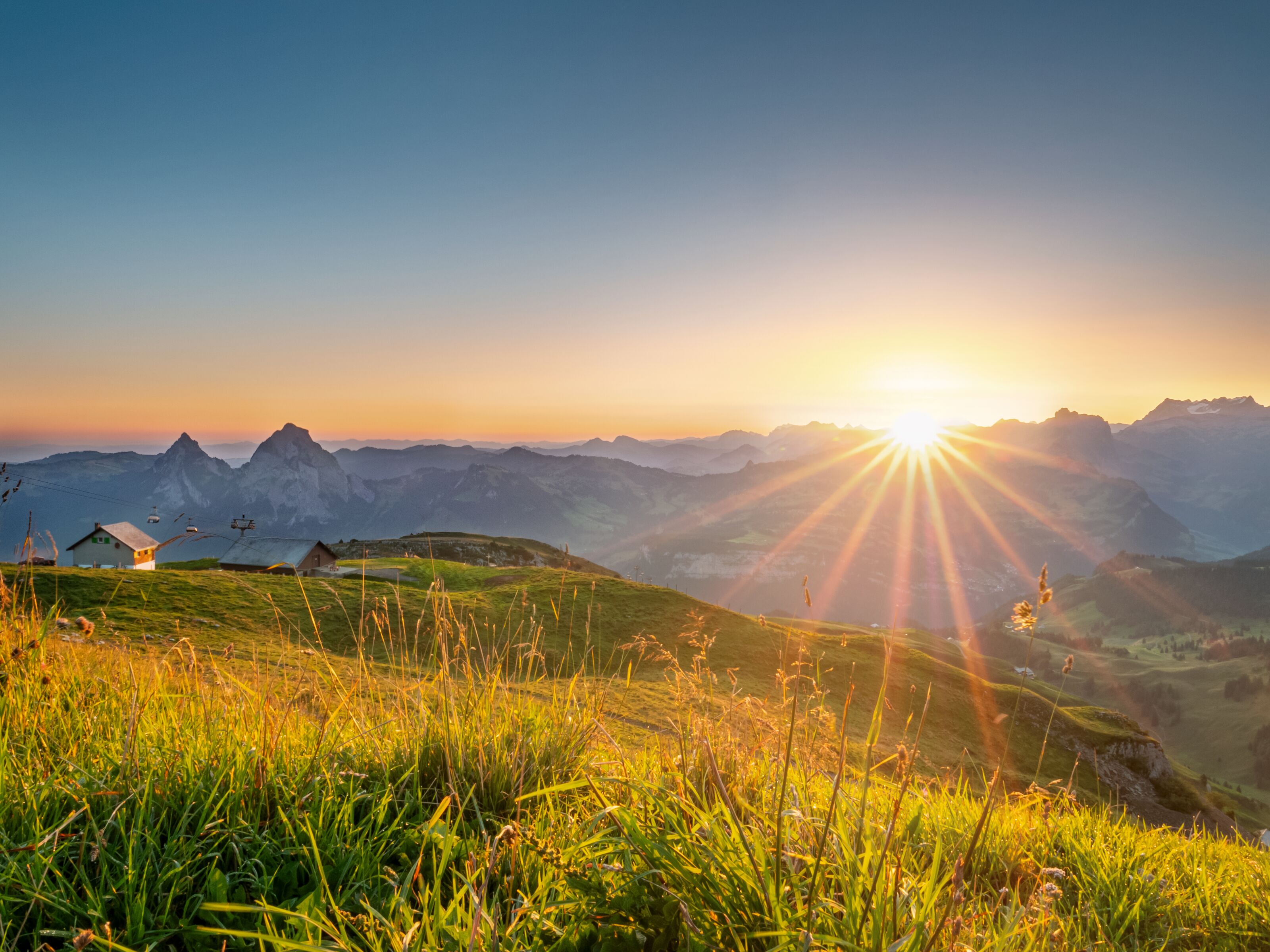 Sonnenaufgang über einer alpinen Berglandschaft mit goldenen Wiesen und Blick auf die umliegenden Gipfel.