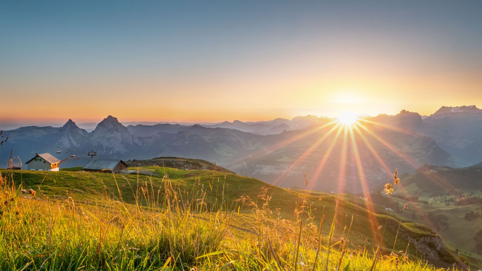 Sonnenaufgang über einer alpinen Berglandschaft mit goldenen Wiesen und Blick auf die umliegenden Gipfel.