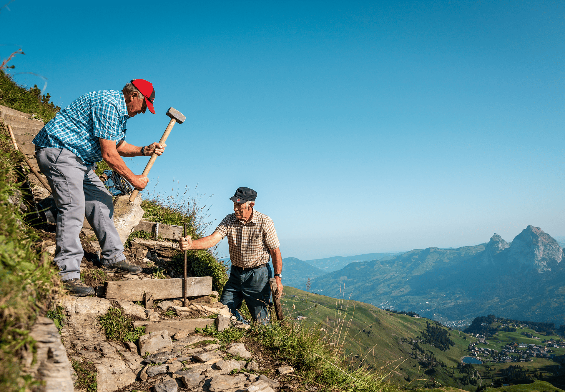 Wanderer steigen über einen steilen Bergpfad mit Stufen und Blick auf die alpine Landschaft.