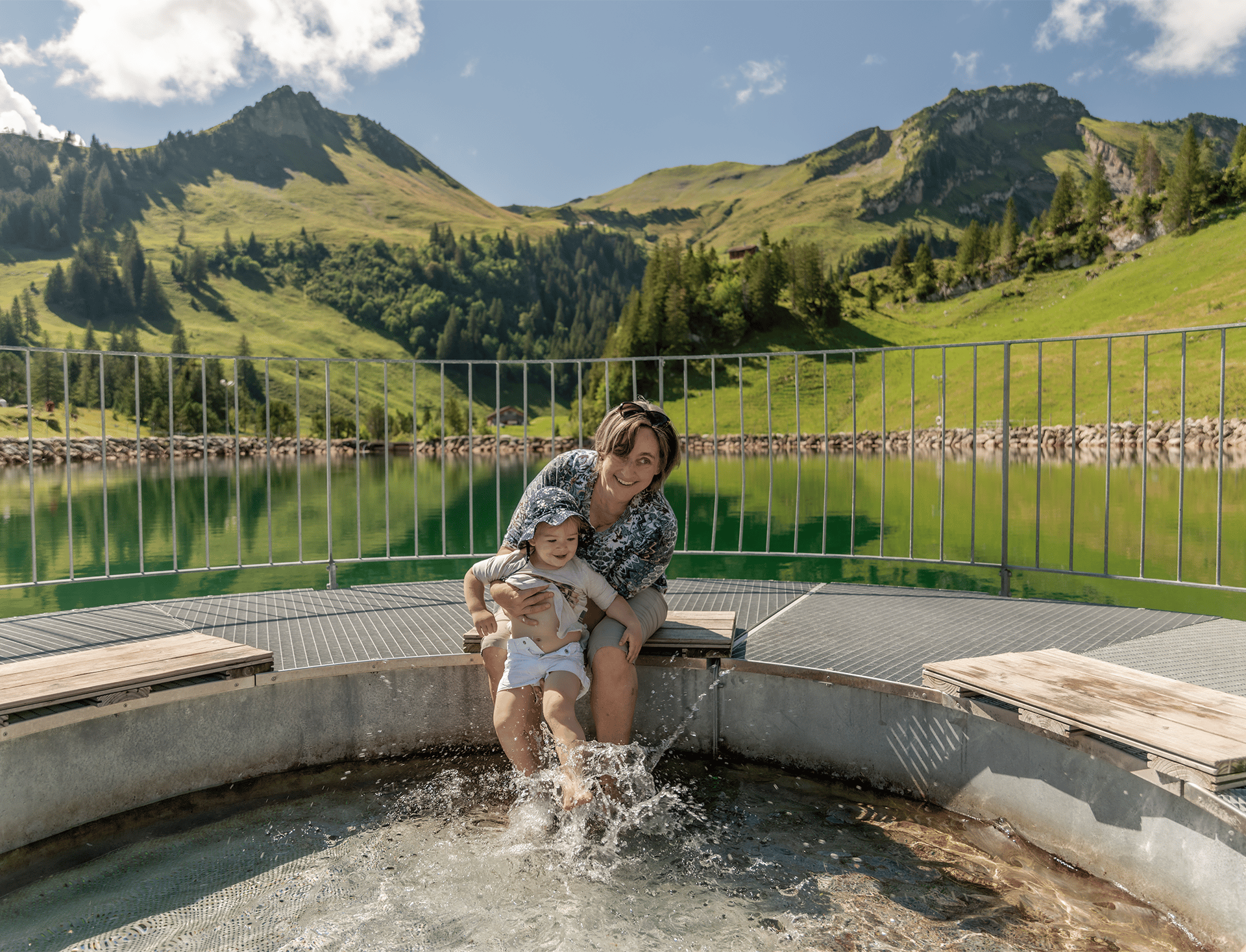 Child sitting at the edge of a mountain lake playing with the water, with views of the alpine landscape.
