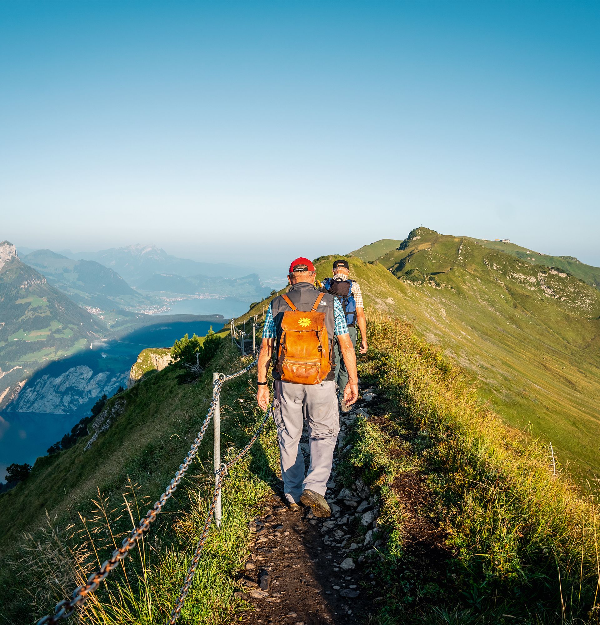 Wanderer auf dem Gratweg zwischen Klingenstock und Fronalpstock mit schmalem Pfad und Blick auf den Vierwaldstättersee und die umliegenden Berge.