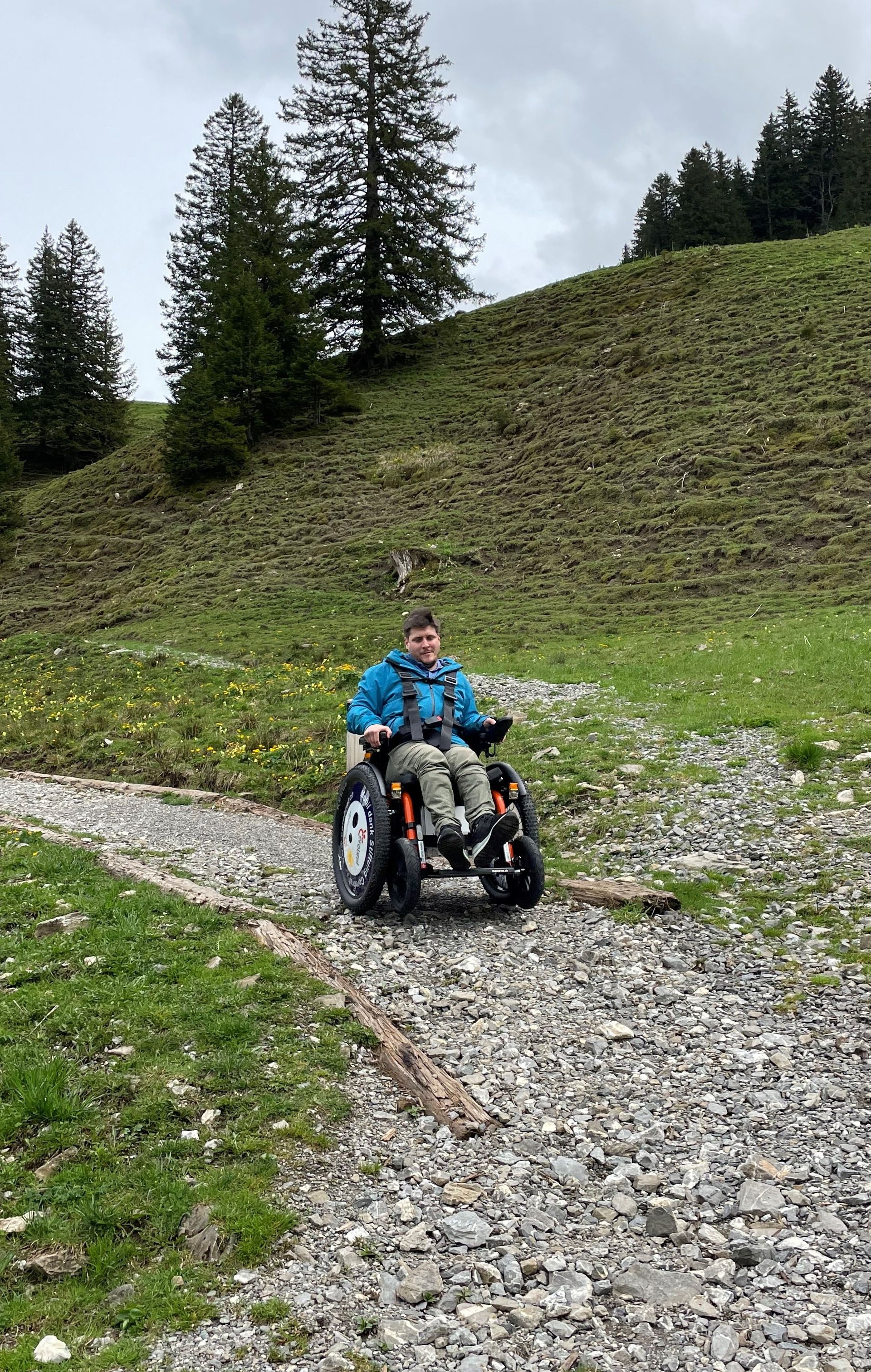 Person fährt mit einem geländegängigen Elektrorollstuhl auf einem Bergweg durch alpine Landschaft.