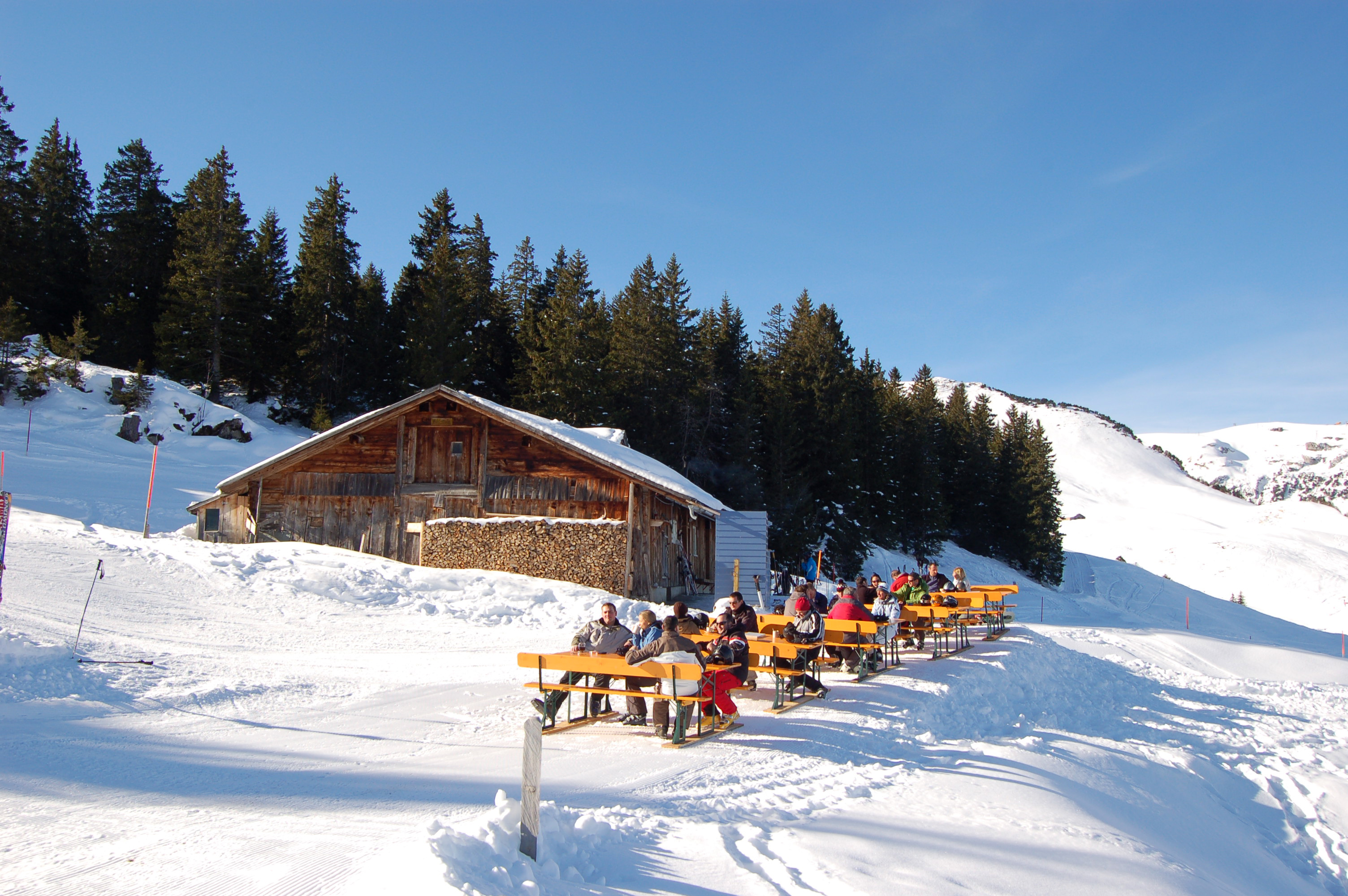 Bergrestaurant mit Terrasse in verschneiter Landschaft, Sitzplätze im Freien unter Sonnenschein.