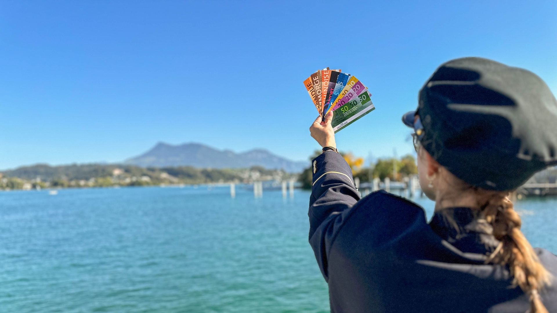 Picture with a person lifting the vouchers into the sky and in the background you can see Lake Lucerne and the mountains.