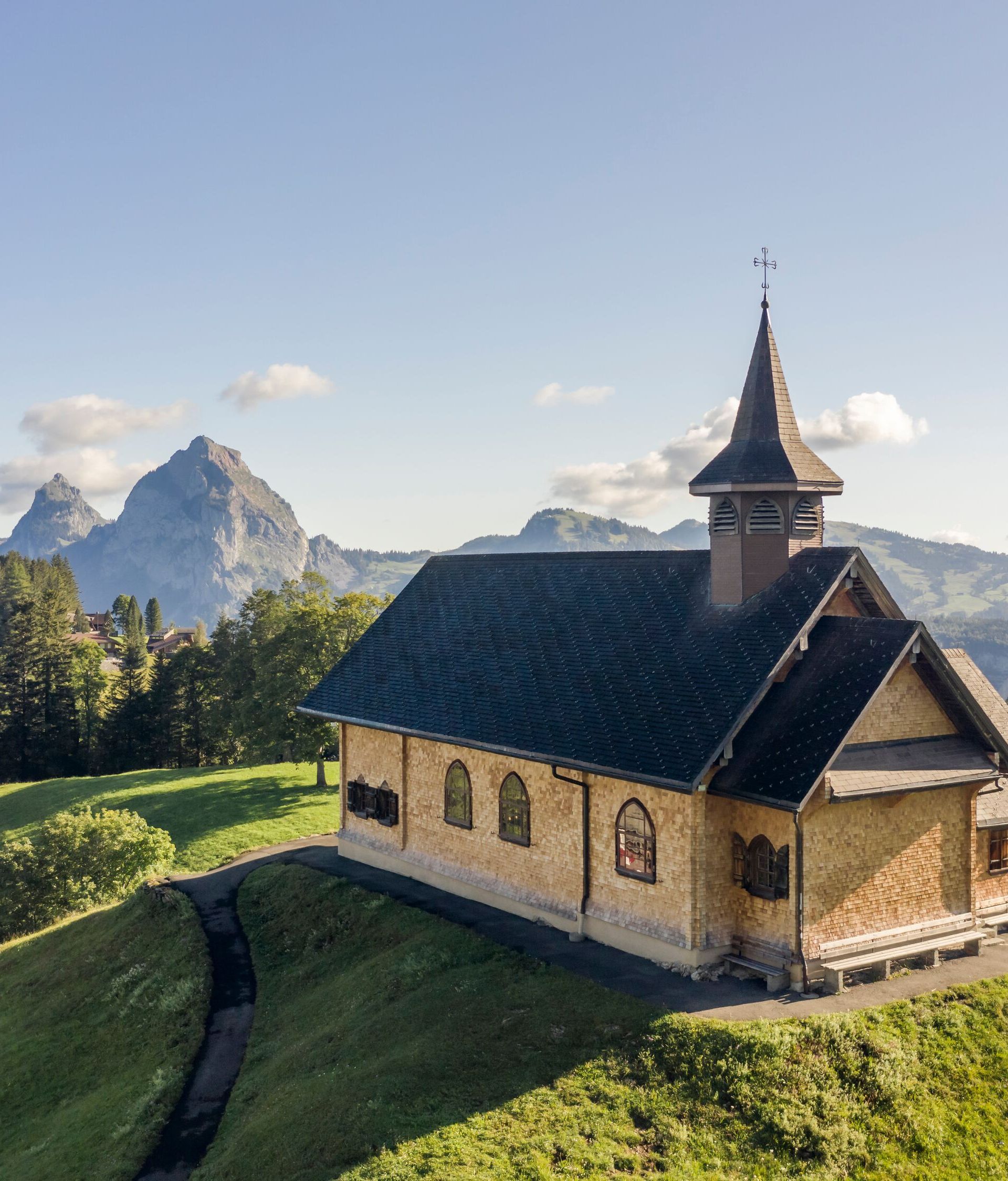 Kapelle auf einem Hügel in alpiner Landschaft mit Blick auf umliegende Berge.