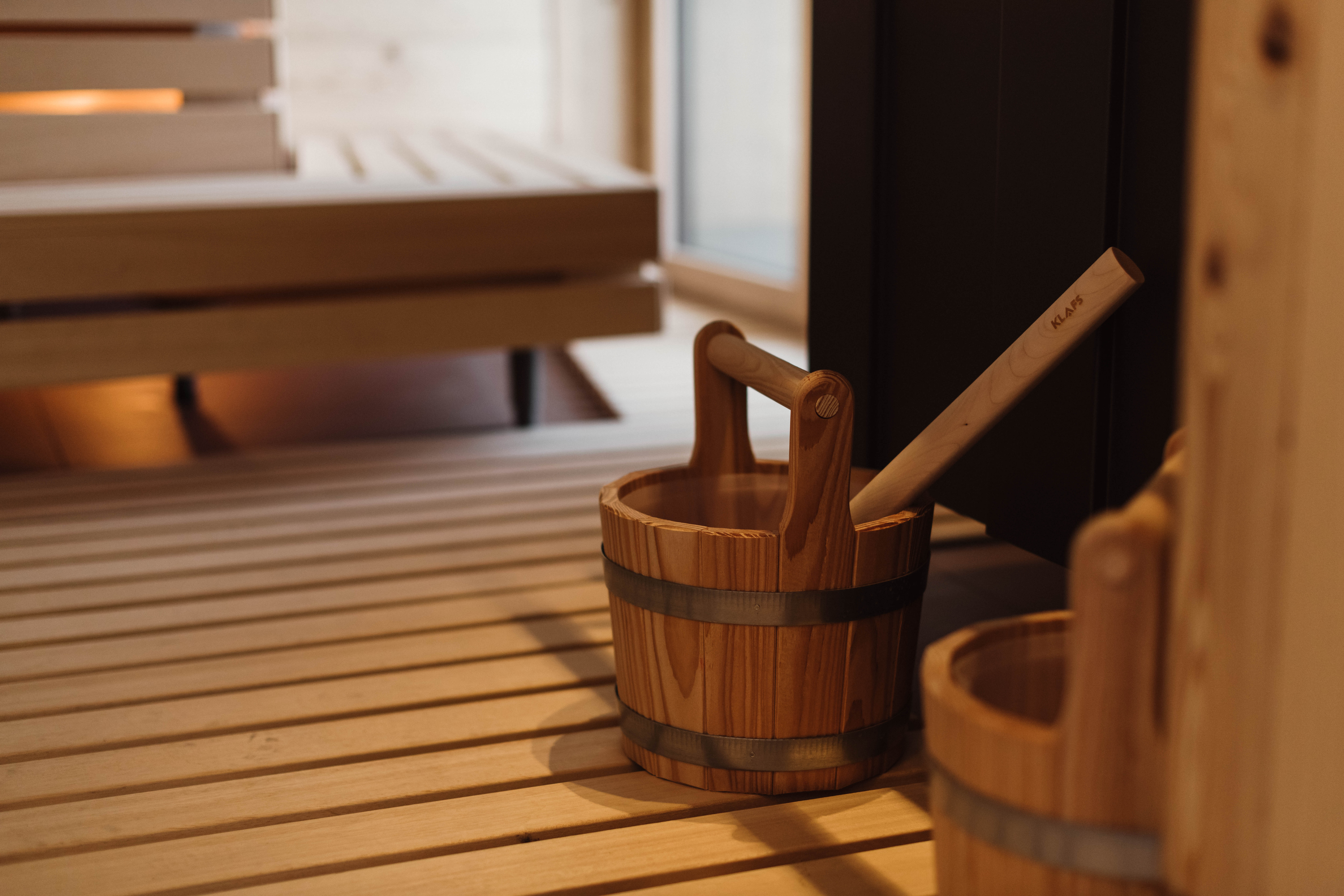 Sauna-Detail mit Holzeimer, Kelle und warm beleuchteten Sitzbänken.