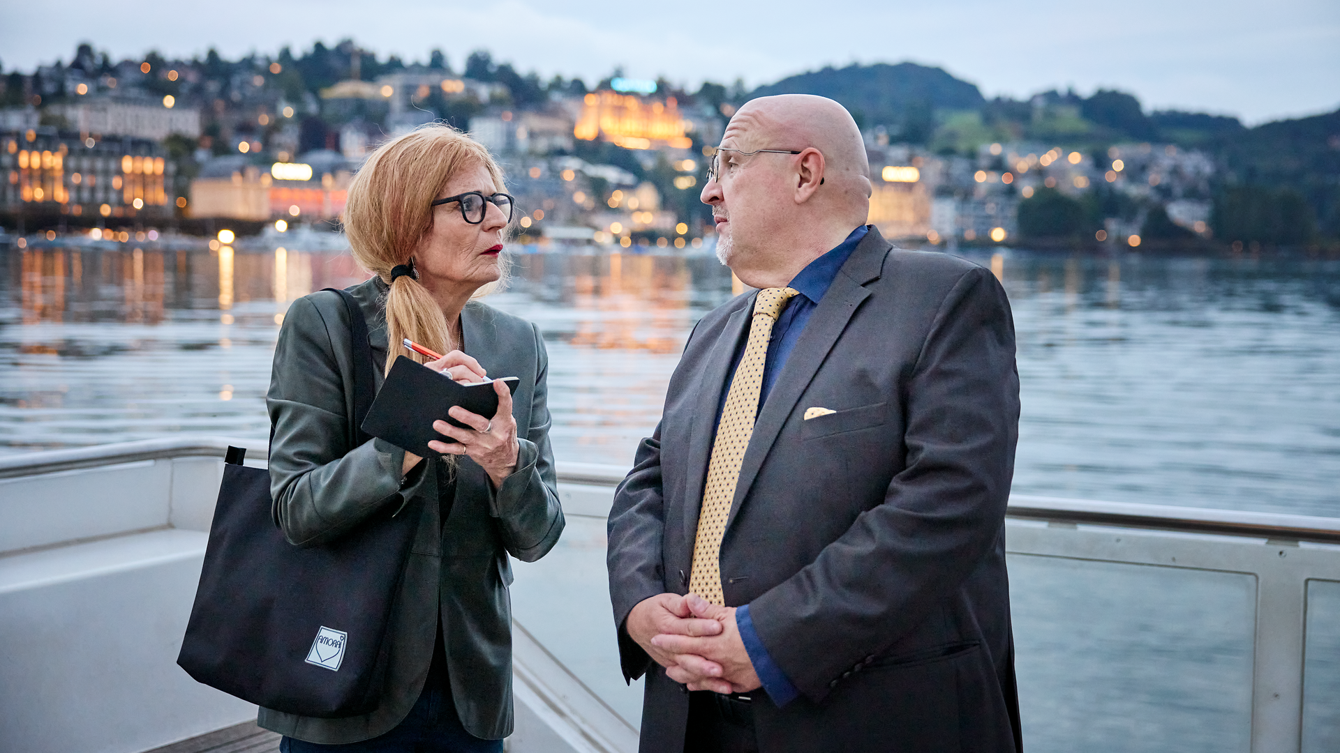 Two people having a serious conversation on the deck of a ship at dusk.