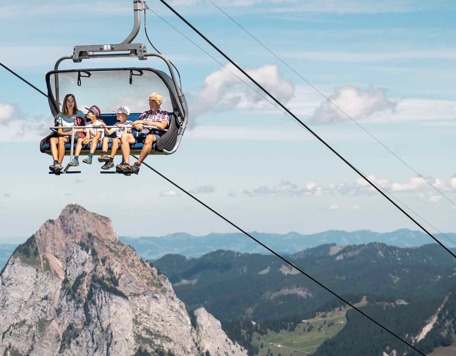 Chairlift at Fronalpstock with passengers above a stunning mountain landscape and distinctive peaks.