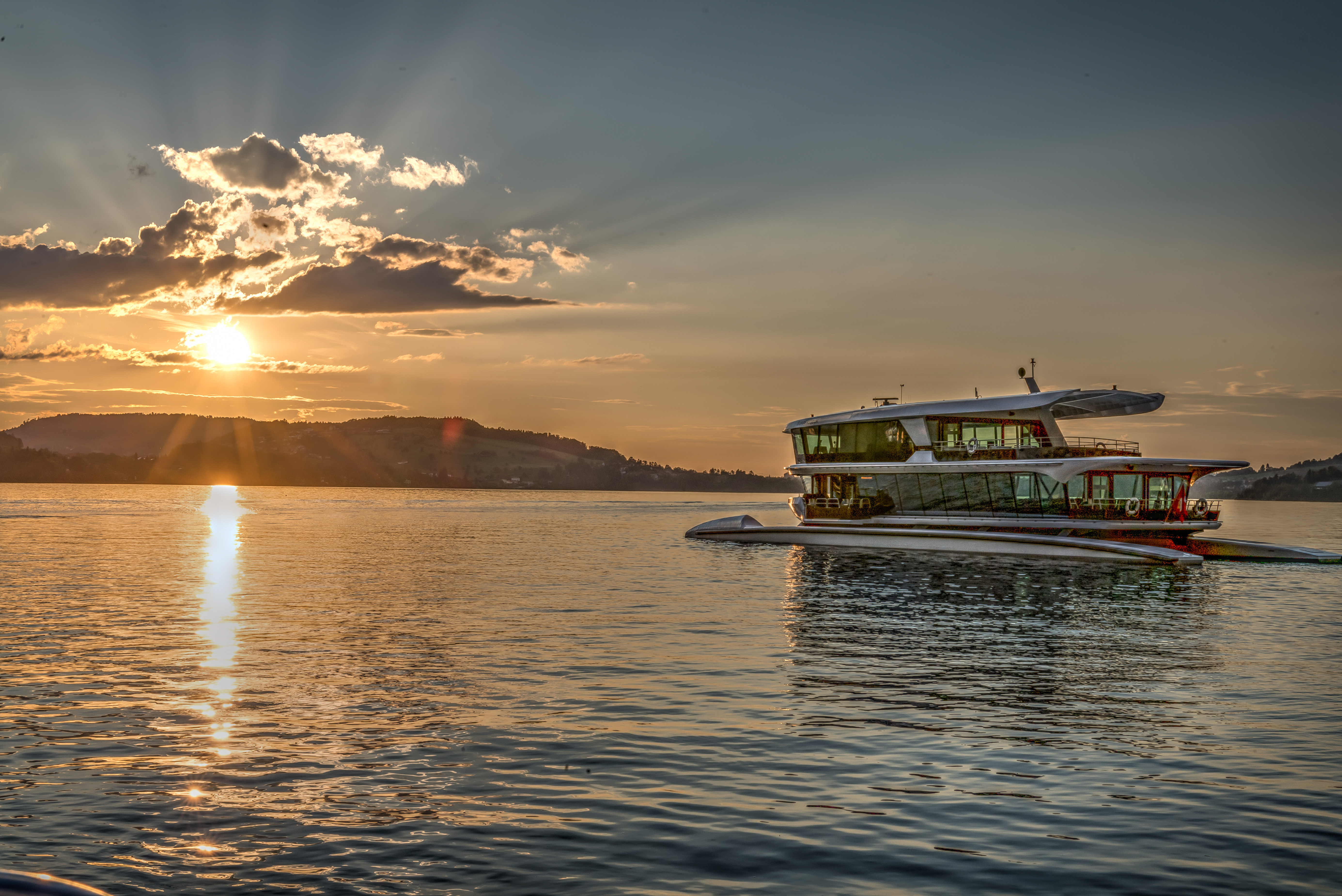 Motorschiff auf dem Vierwaldstättersee bei Sonnenaufgang mit goldenem Licht und Bergpanorama