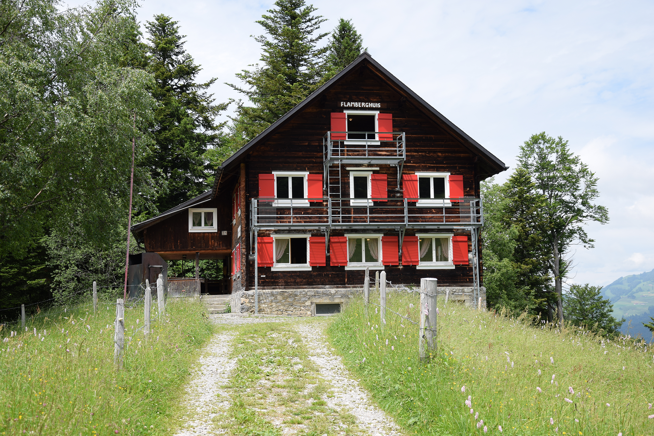 Traditionelles Berghaus mit roten Fensterläden auf einer Wiese in alpiner Umgebung.