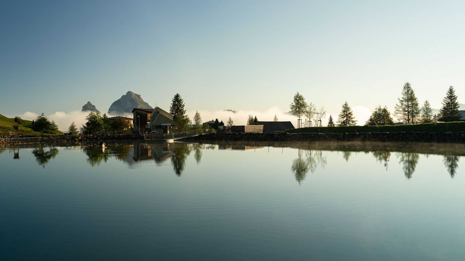 Mountain lake with a calm surface reflecting houses and trees in an alpine landscape.
