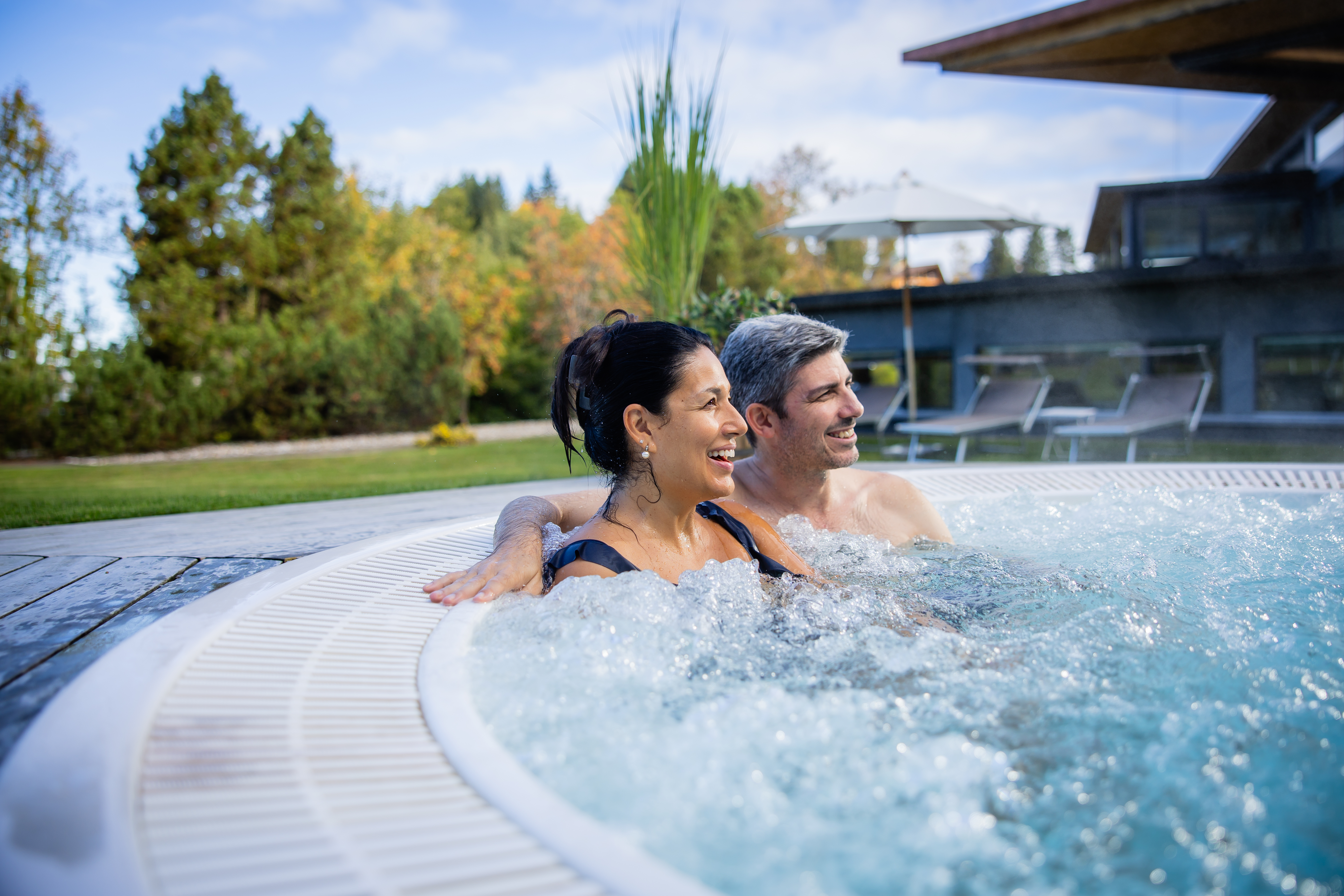 Two people relaxing in a warm outdoor hot tub with a view of greenery