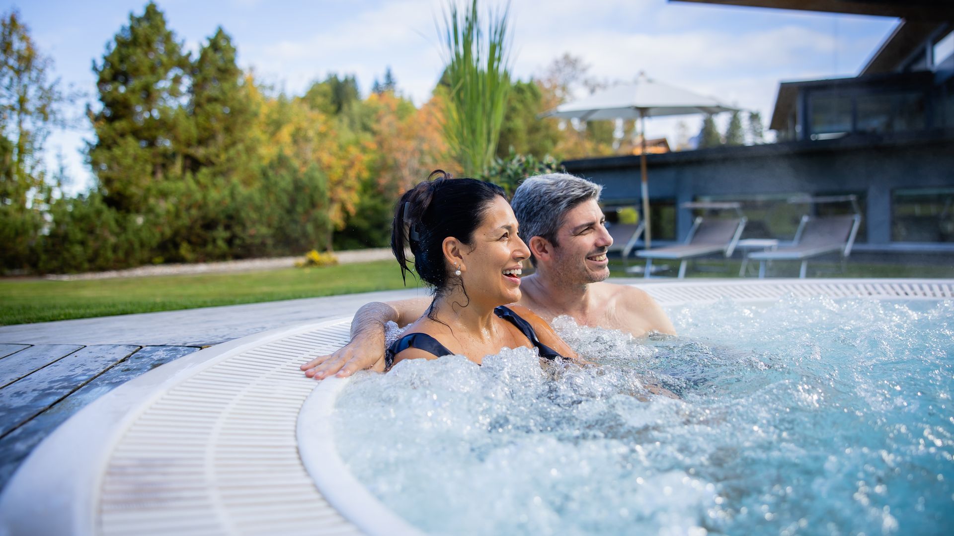 Two people relaxing in a warm outdoor hot tub with a view of greenery