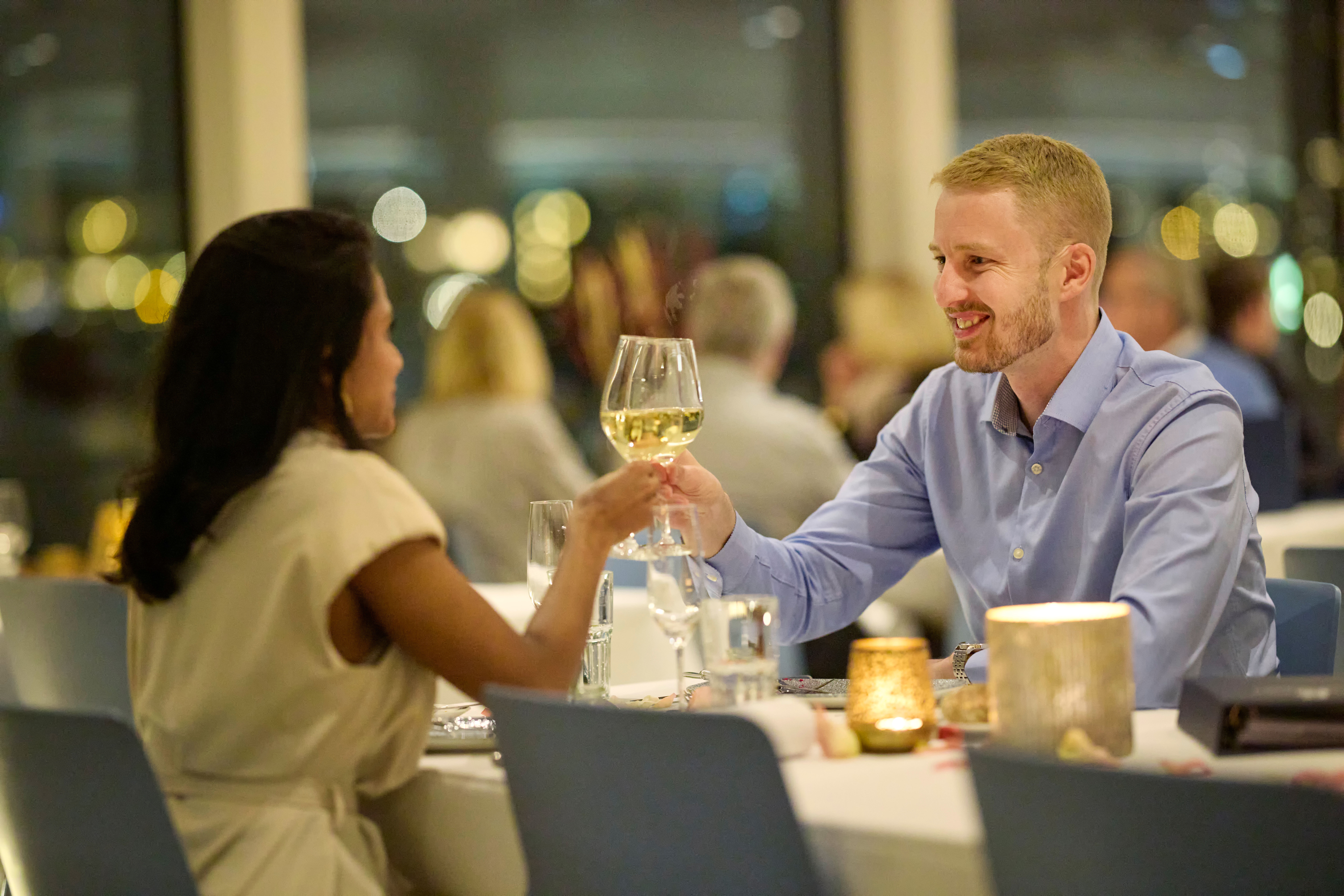 Paar stösst mit Weingläsern bei Kerzenlicht an einem Tisch im Innenraum eines Schiffes an.