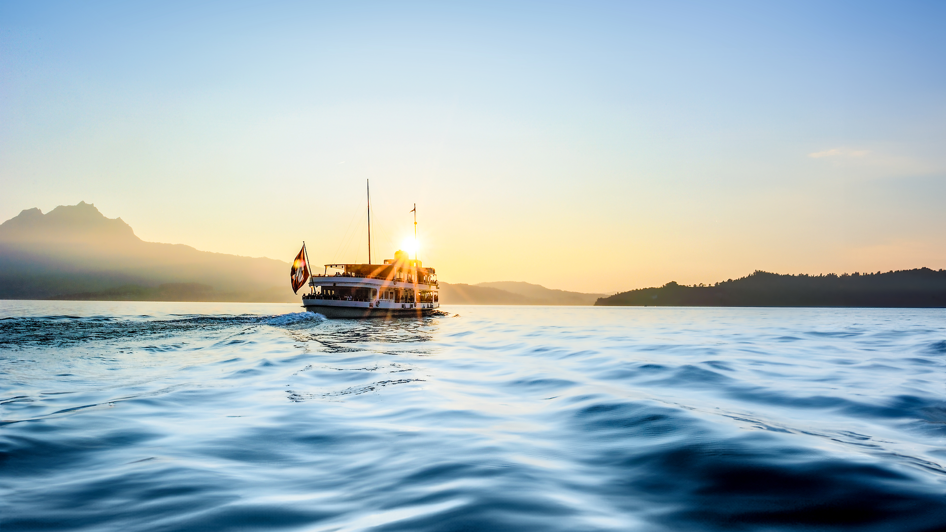 Bateau naviguant sur le lac des Quatre-Cantons au coucher du soleil avec montagnes en arrière-plan.