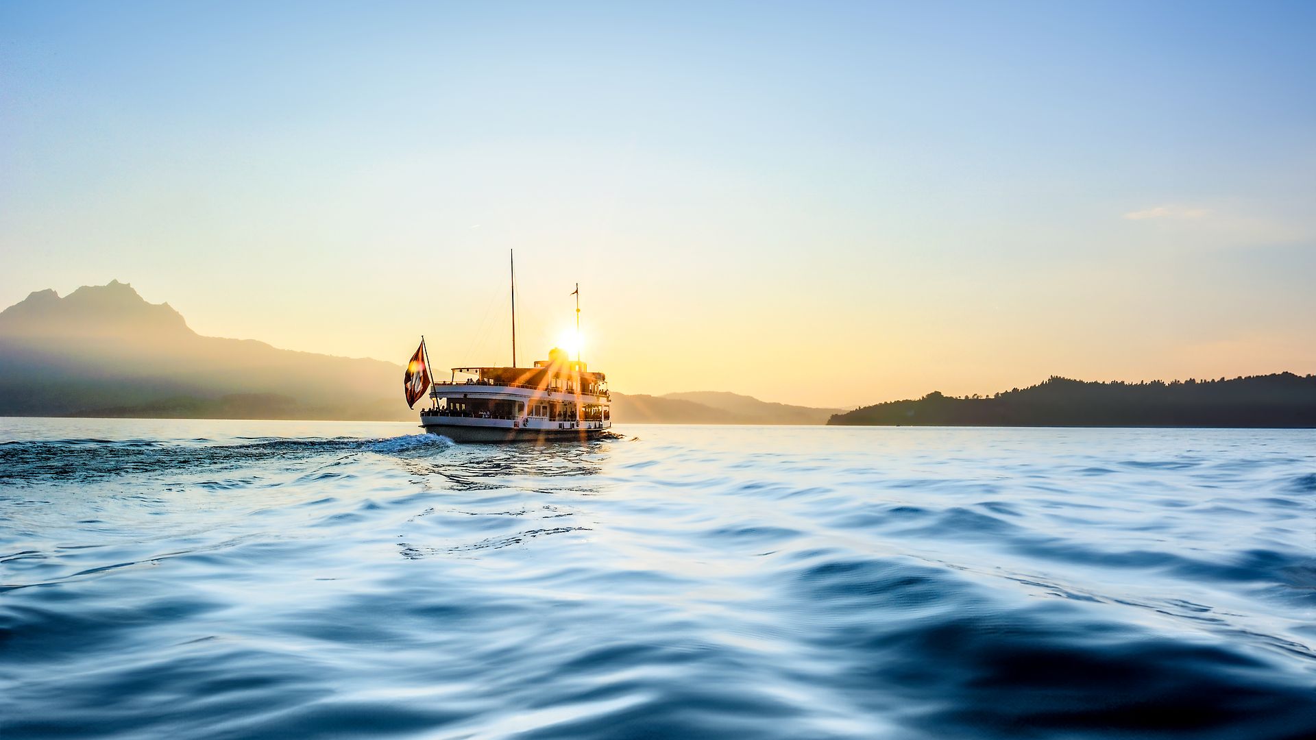 Bateau naviguant sur le lac des Quatre-Cantons au coucher du soleil avec montagnes en arrière-plan.