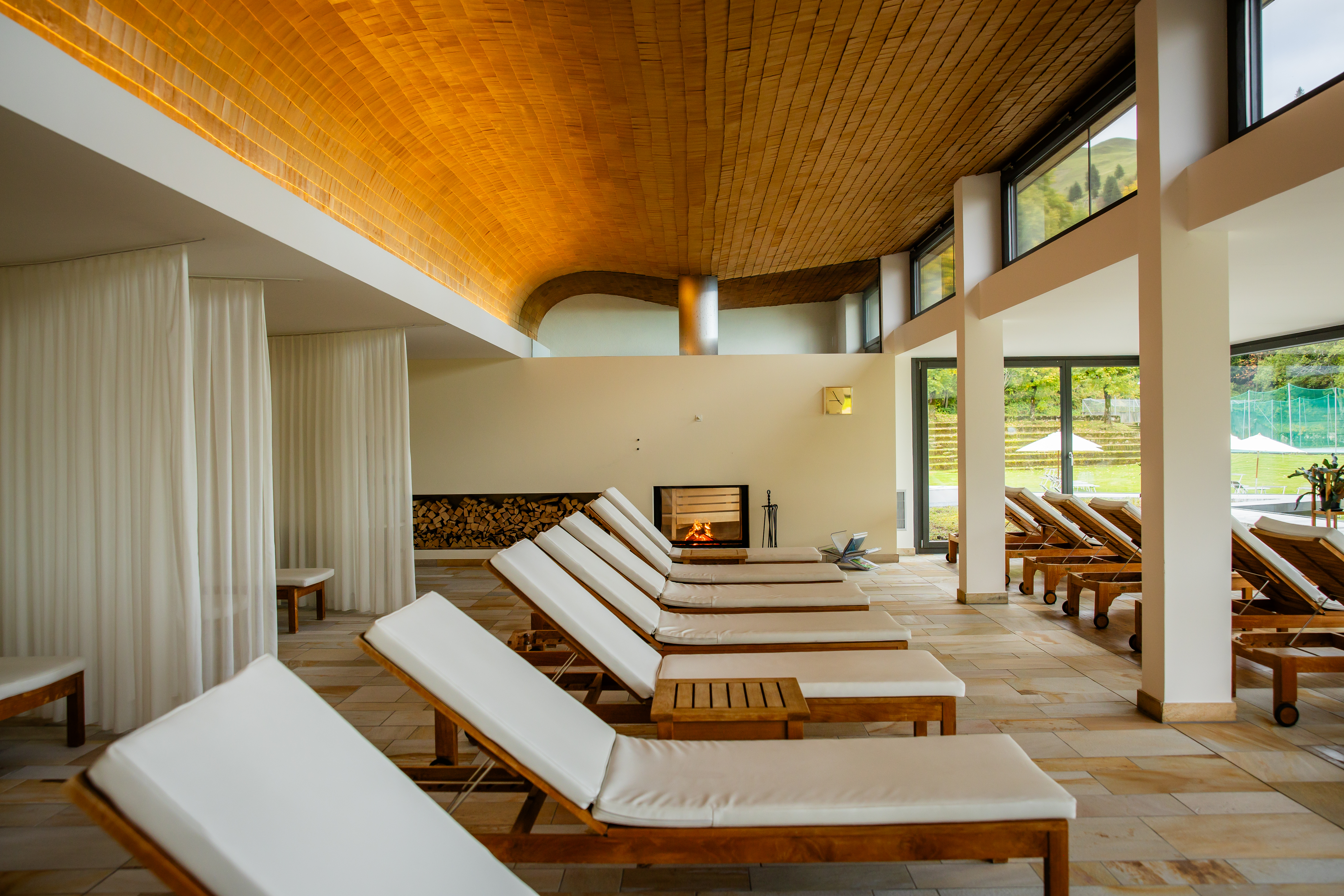 Bright relaxation room with loungers, fireplace, and large windows overlooking the outdoors.