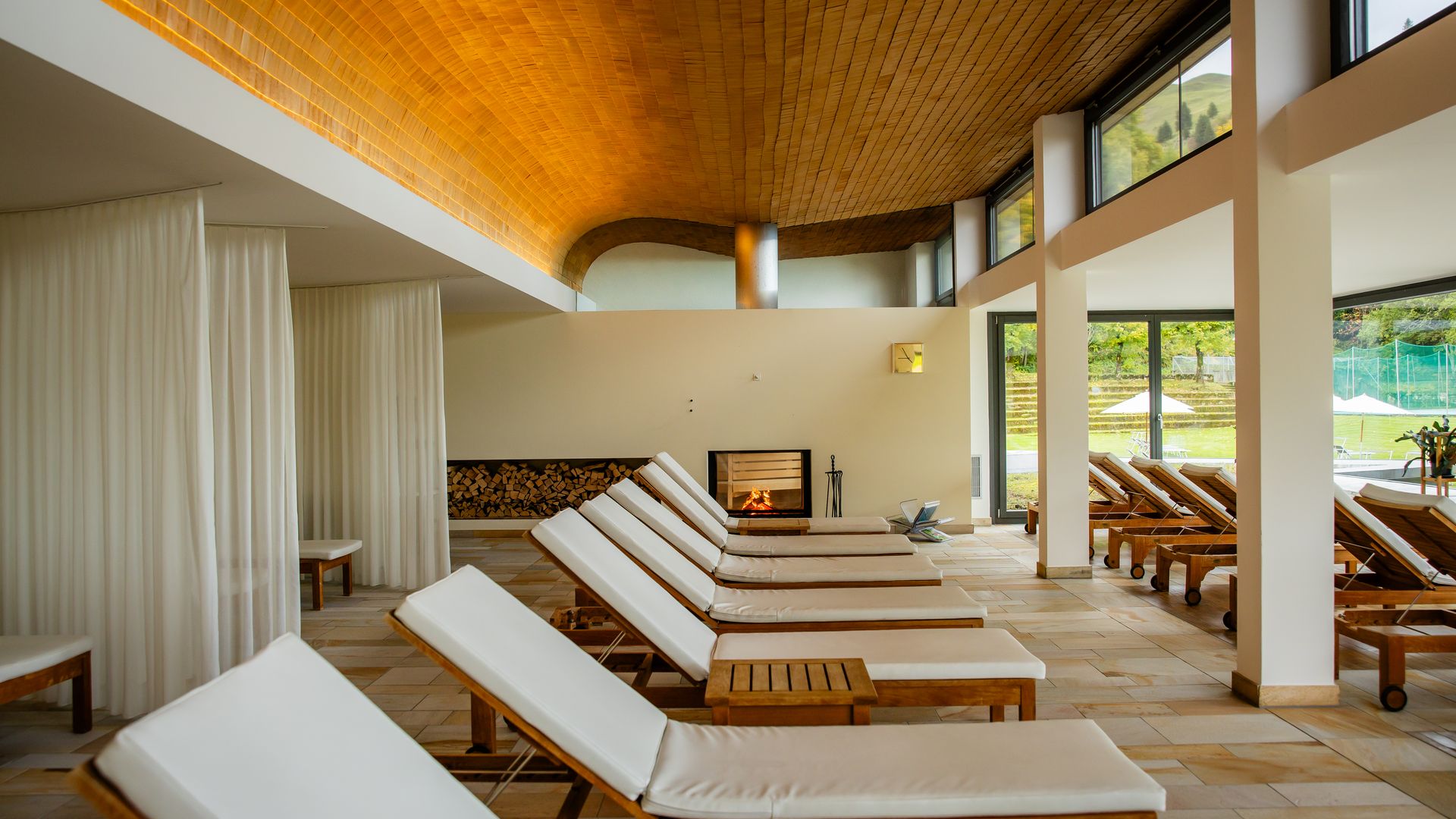 Bright relaxation room with loungers, fireplace, and large windows overlooking the outdoors.