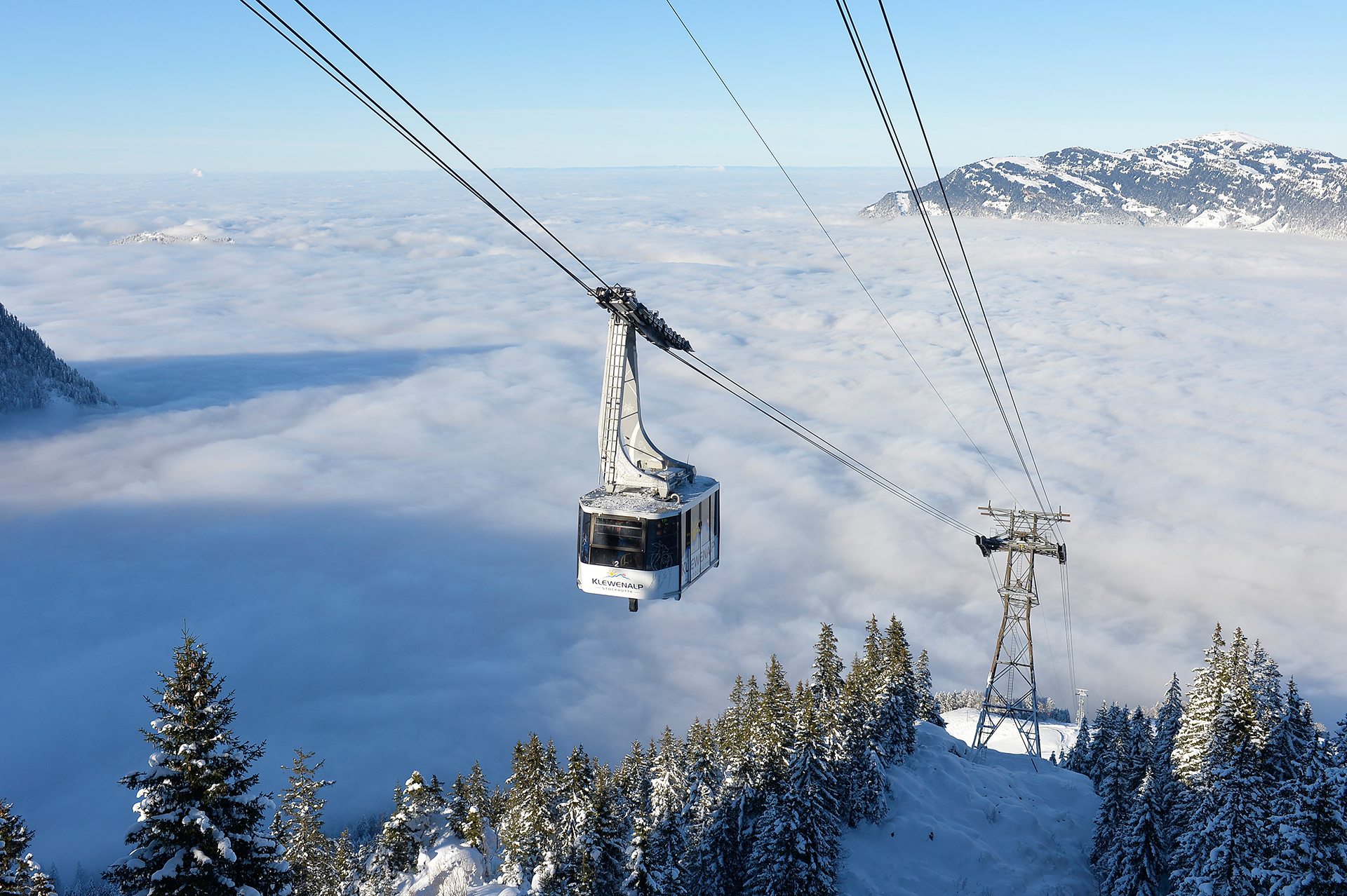 Vue hivernale de la Klewenalp sur une mer de brouillard, y compris le téléphérique qui monte.