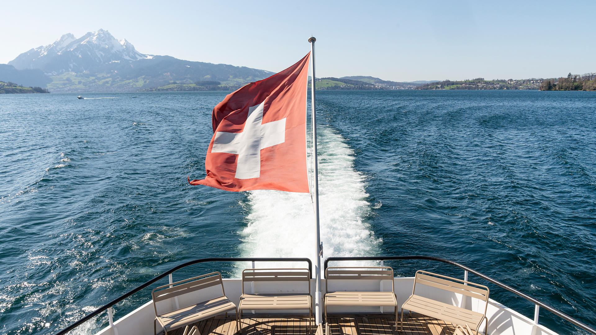 Swiss flag at the stern of a vessel on Lake Lucerne with panoramic views of the lake and surrounding mountains