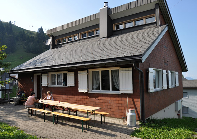 Mountain lodge with benches in front of the building in an alpine setting.